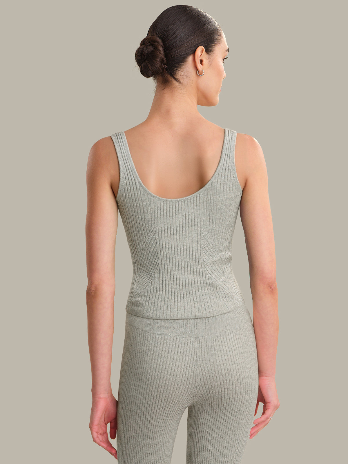 Woman wearing a green ribbed tank top and leggings against a gray background