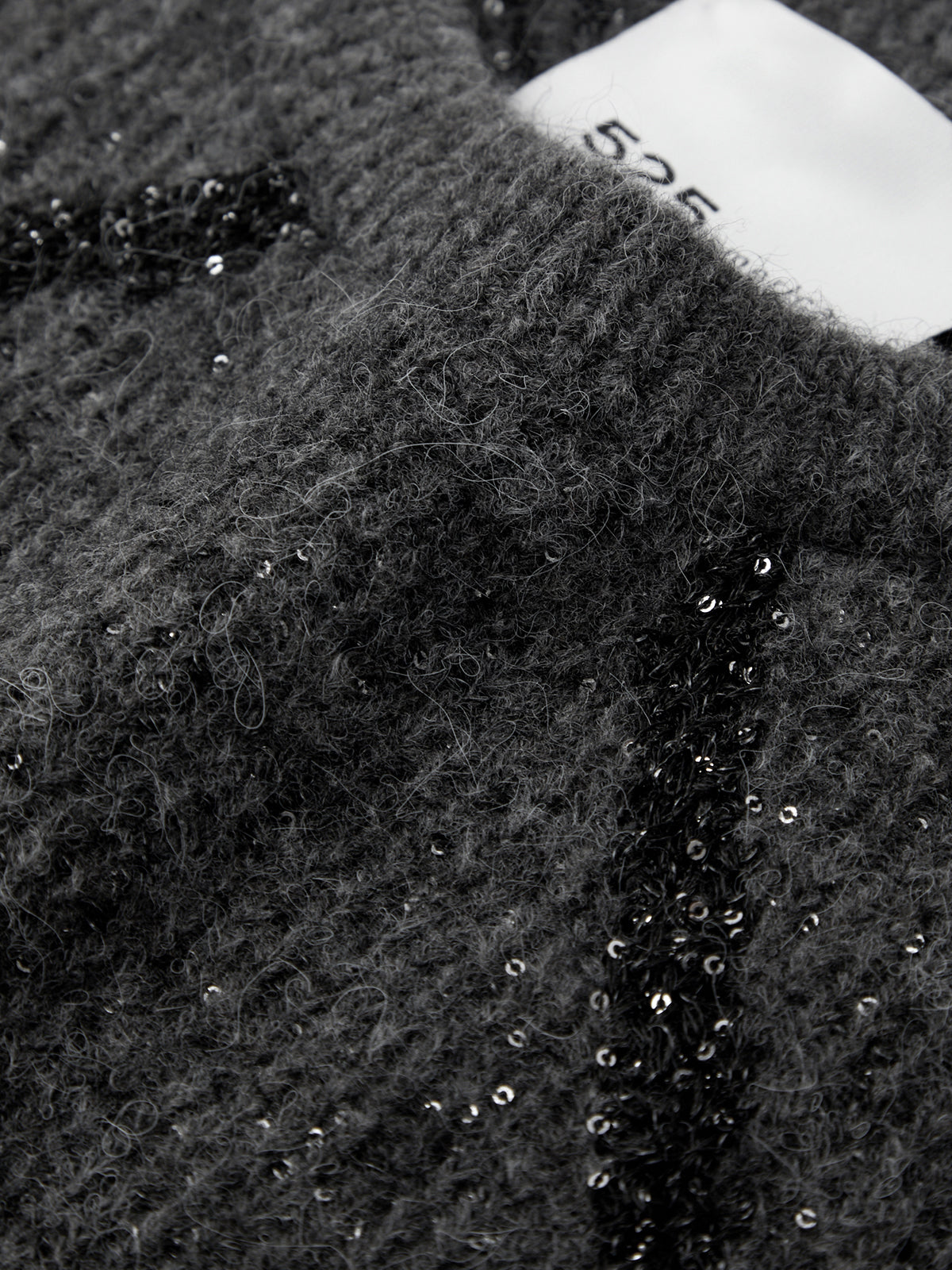 Close-up of a textured fabric with sequins and a brand label.