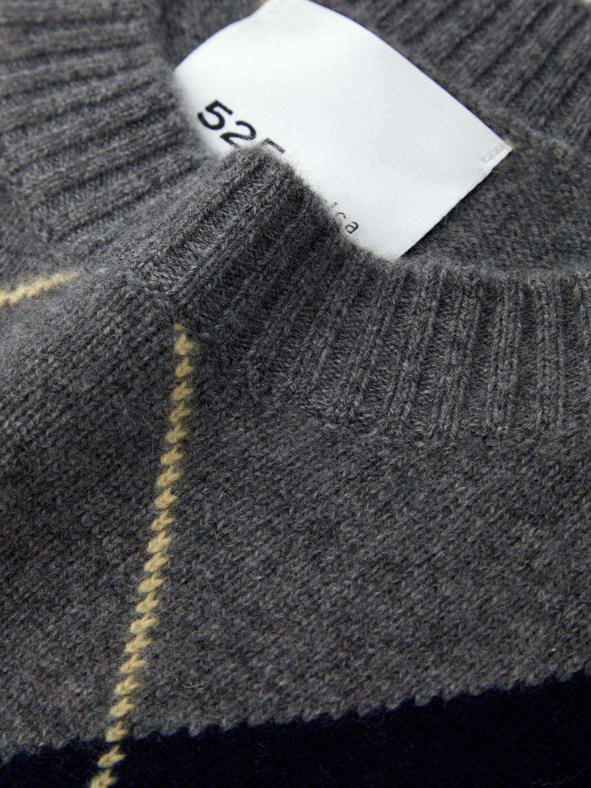 Close-up of a gray sweater with a brand label and yellow stitching detail.
