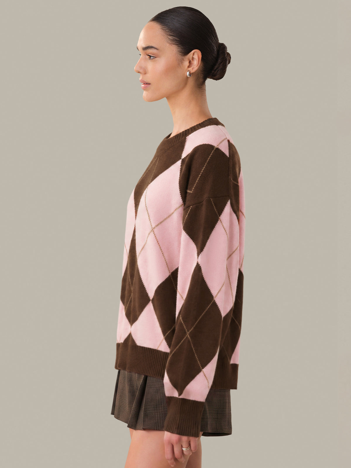 Woman wearing a brown and pink argyle sweater on a neutral background