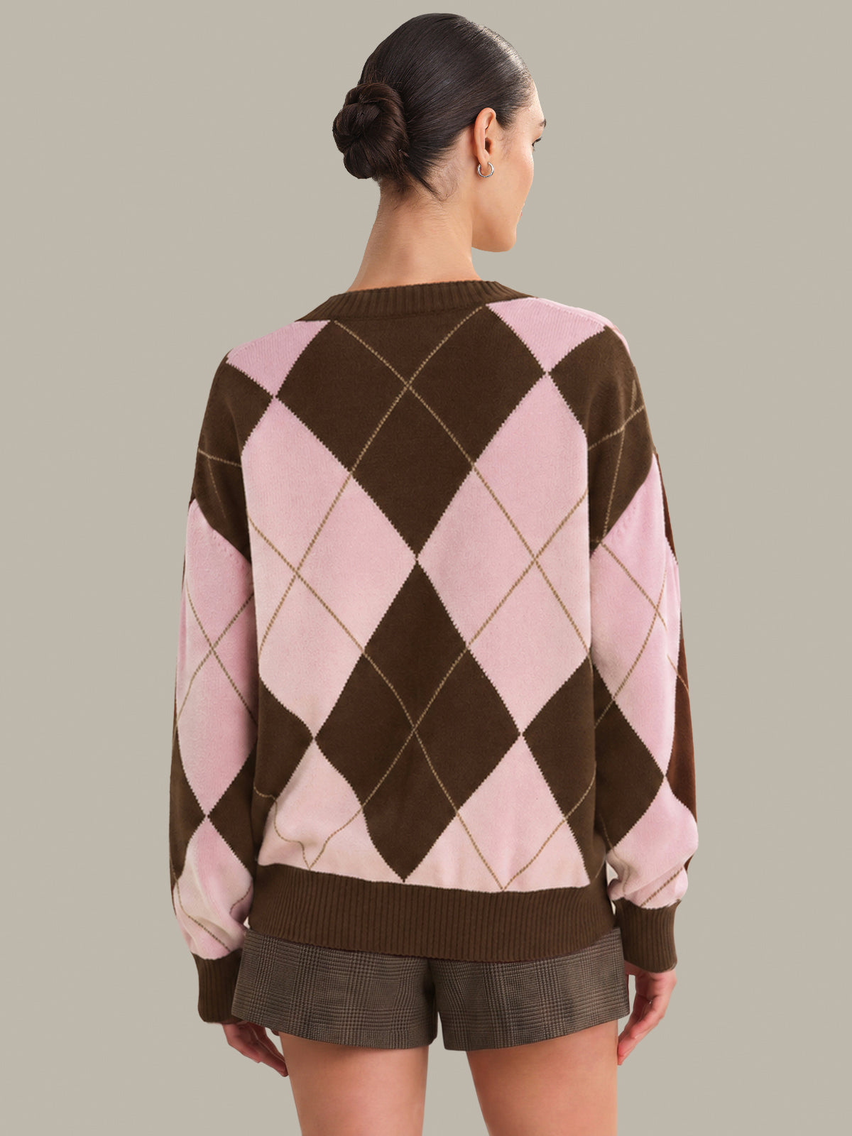 Person wearing a brown and pink argyle sweater with shorts on a plain background