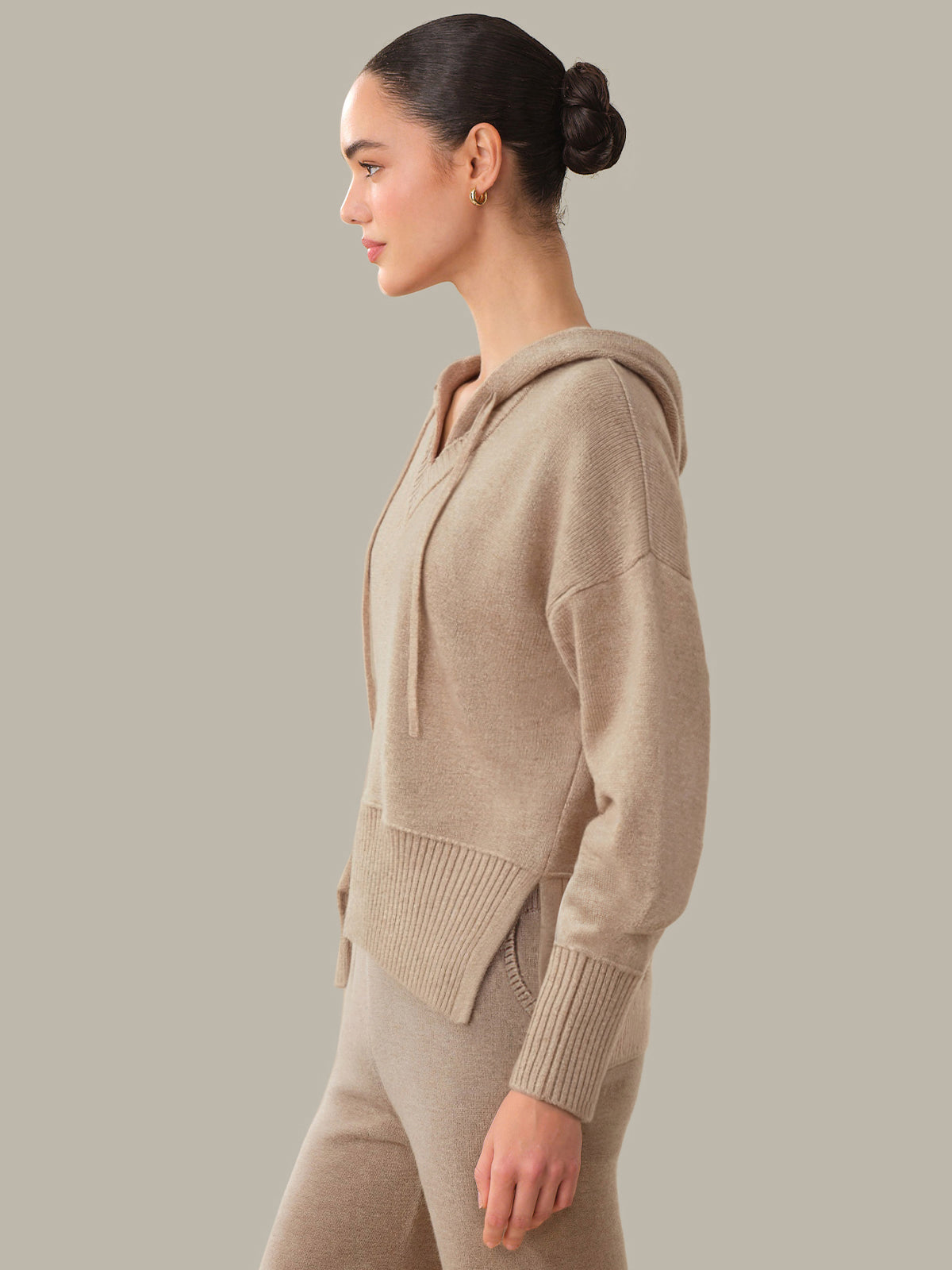 Woman wearing a beige hoodie and pants against a plain background