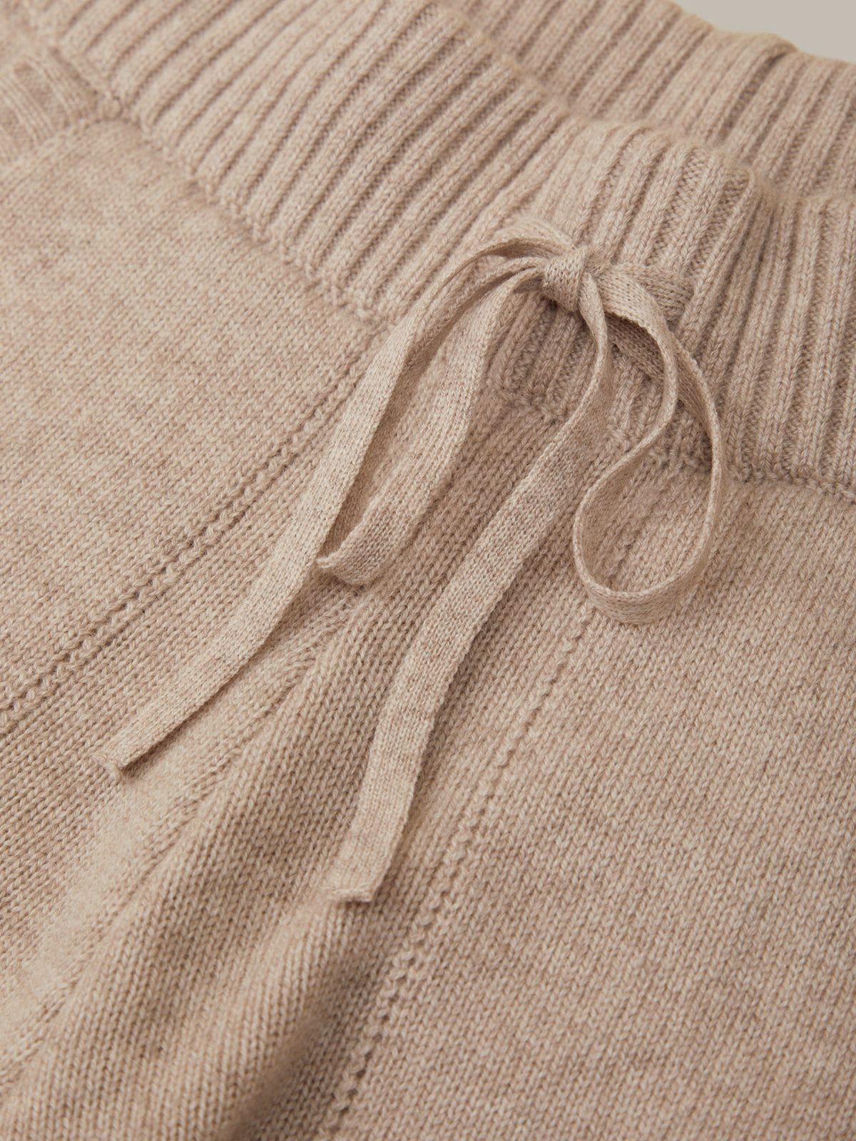Close-up of a beige knitted sweater with a drawstring detail.