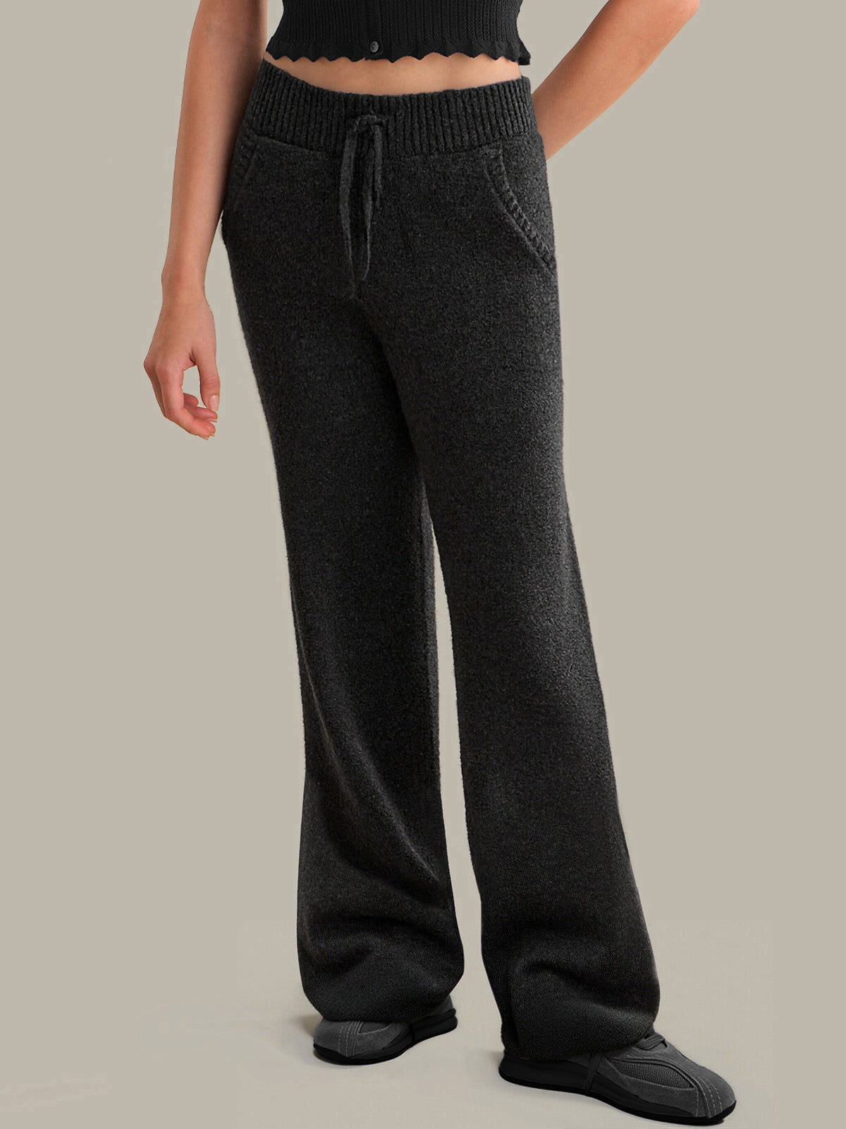 Person wearing dark grey knit pants on a plain background