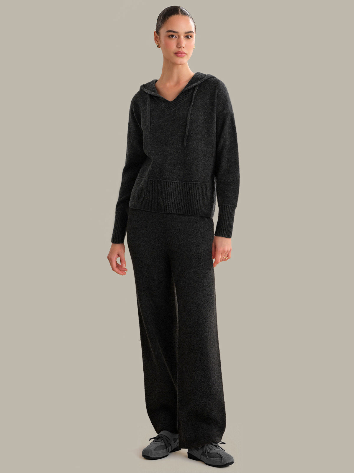 Person wearing a dark gery hoodie and pants on a gray background