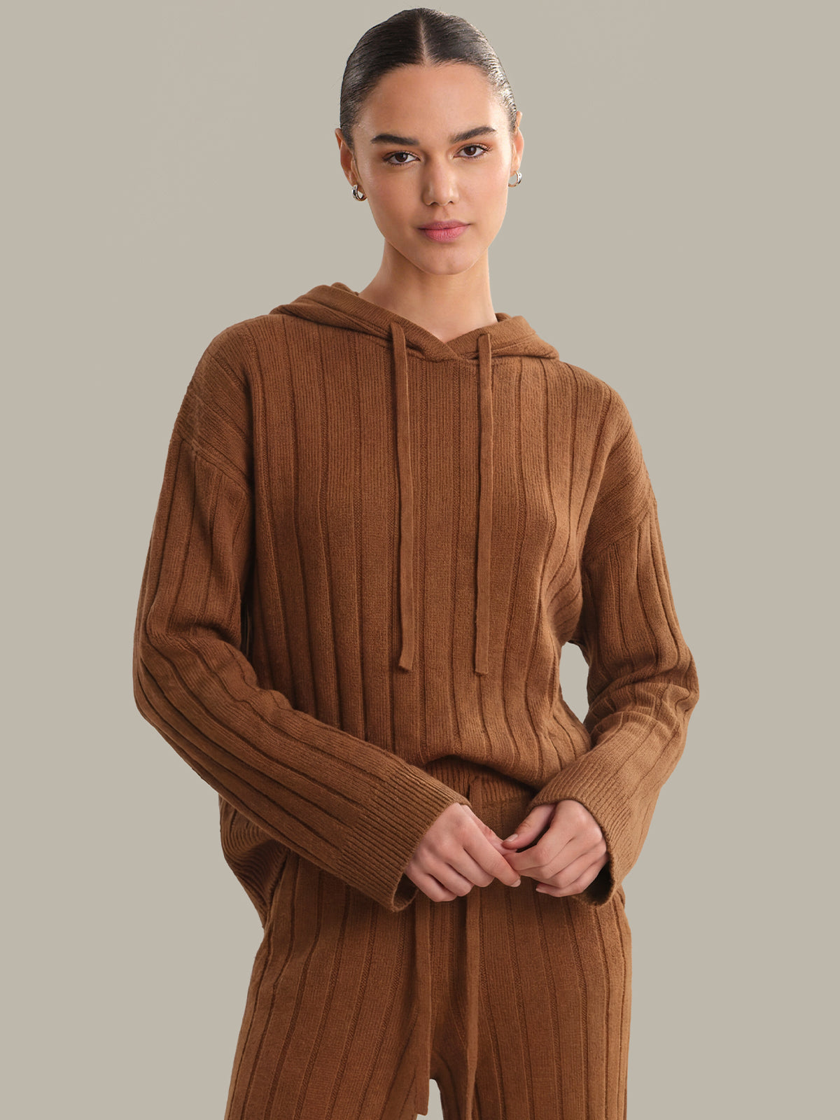 Person wearing a brown ribbed knit hoodie and pants on a neutral background
