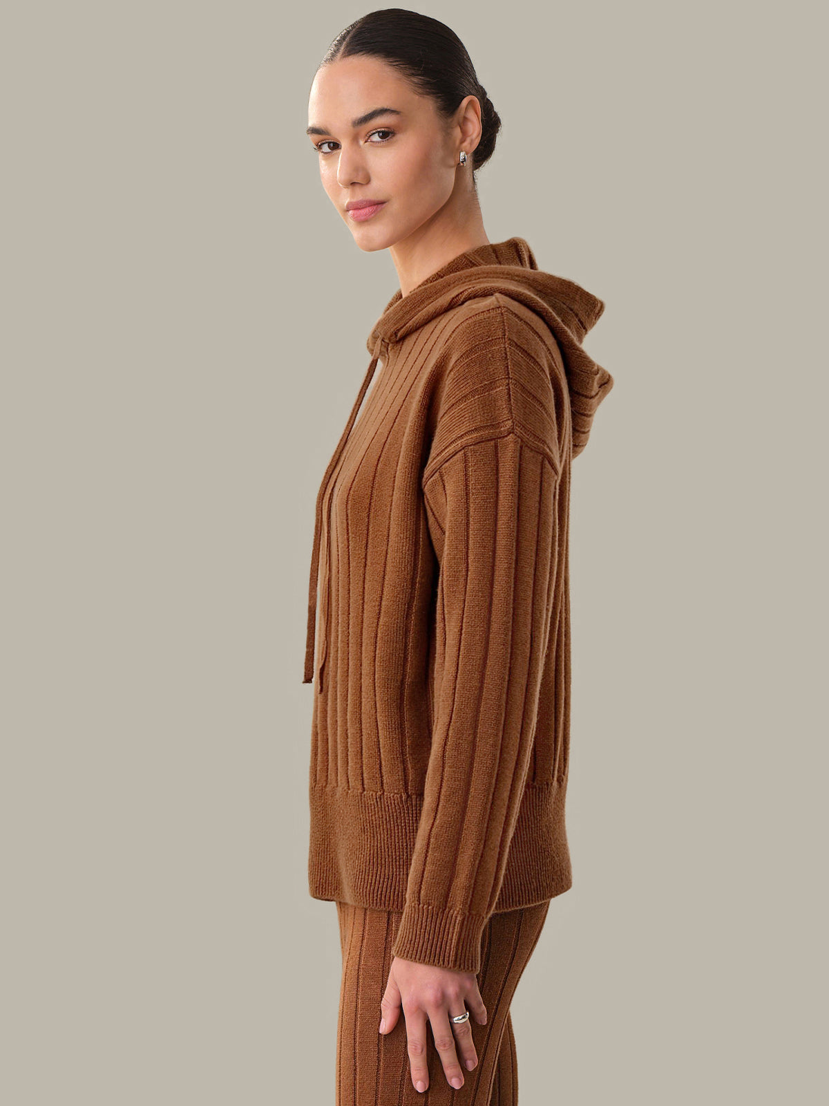 Woman wearing a brown knitted hoodie and pants on a plain background
