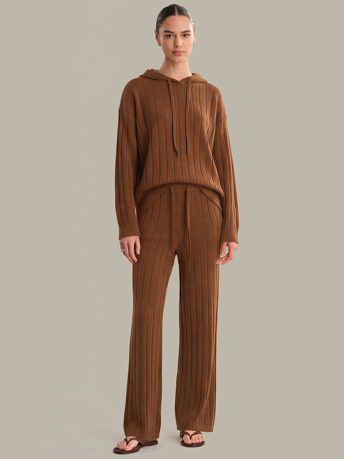 Woman wearing a brown ribbed hoodie and pants on a plain background