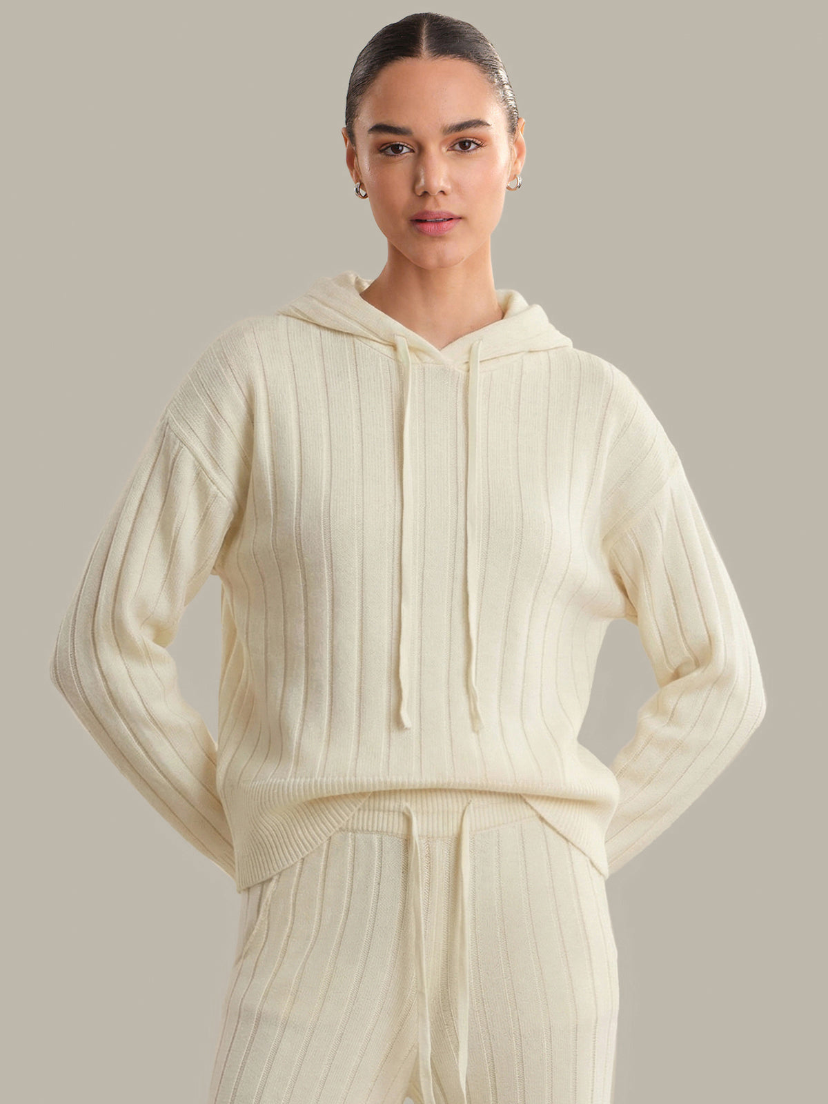 Woman wearing a cream-colored ribbed hoodie and pants on a neutral background