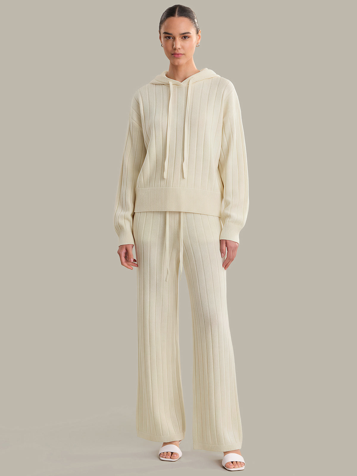 Woman wearing a cream-colored outfit with wide-leg pants on a plain background