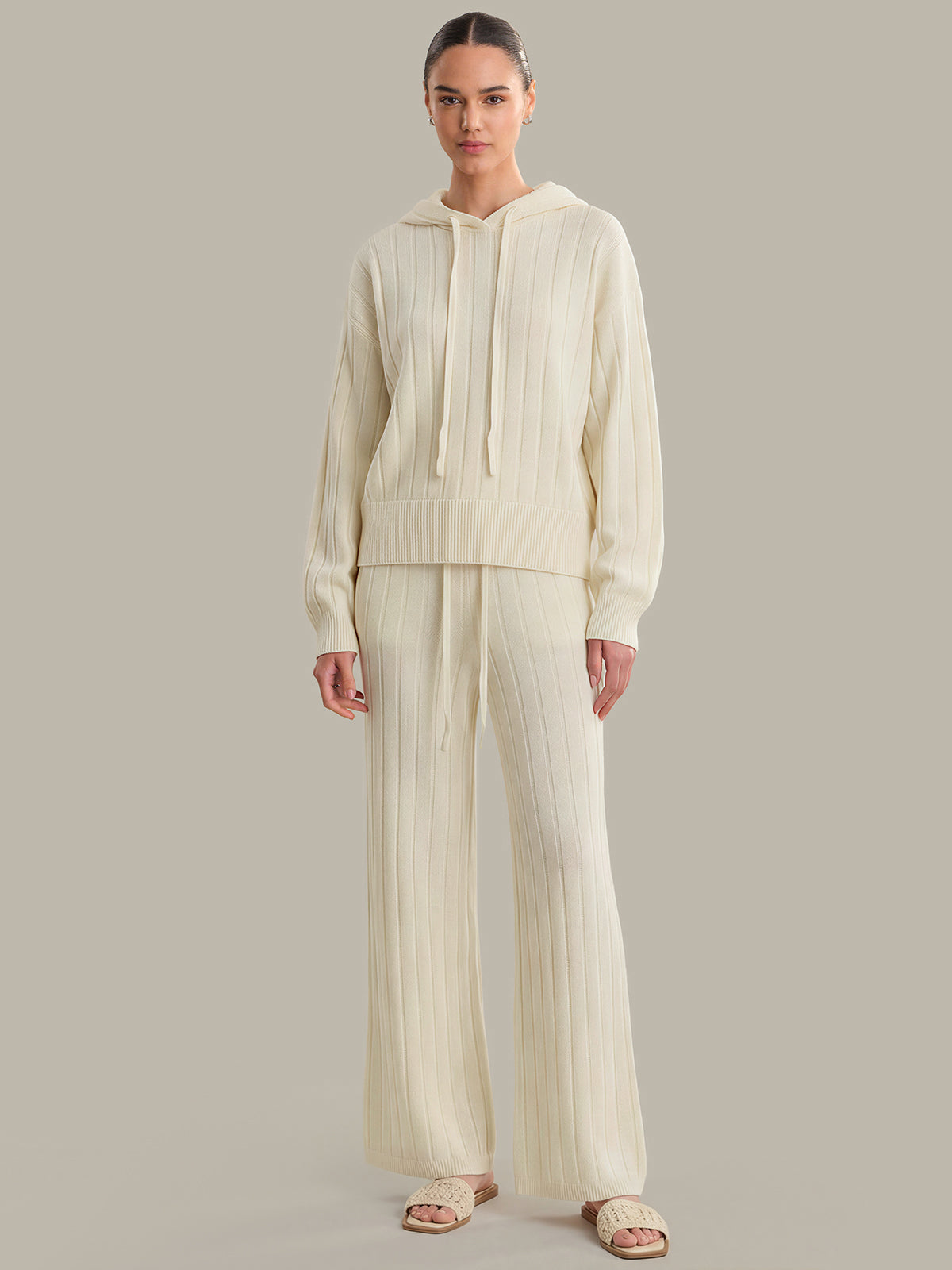 Woman wearing a cream-colored outfit with wide-leg pants on a neutral background