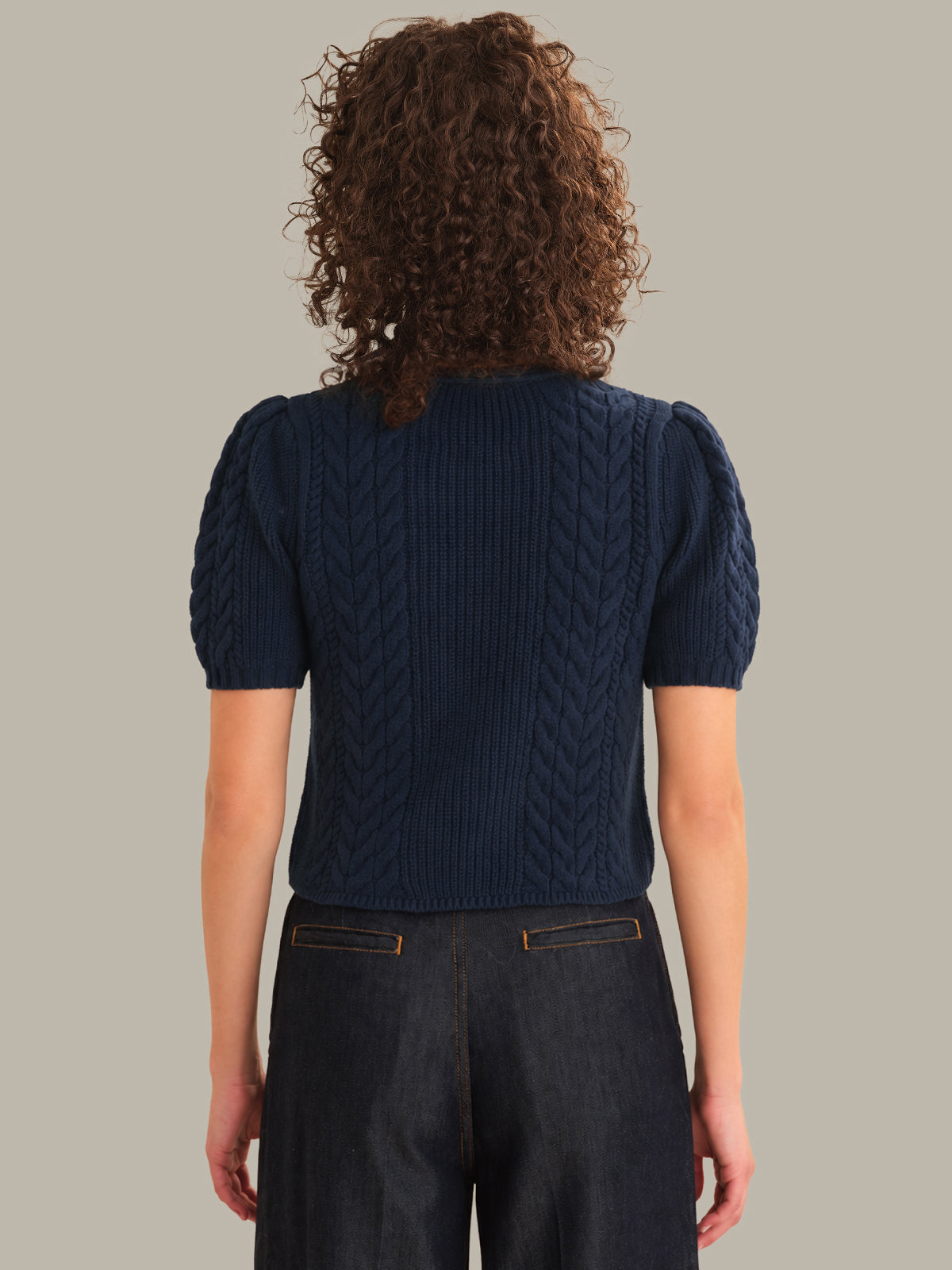 Person wearing a navy blue cable knit top with short sleeves on a plain background