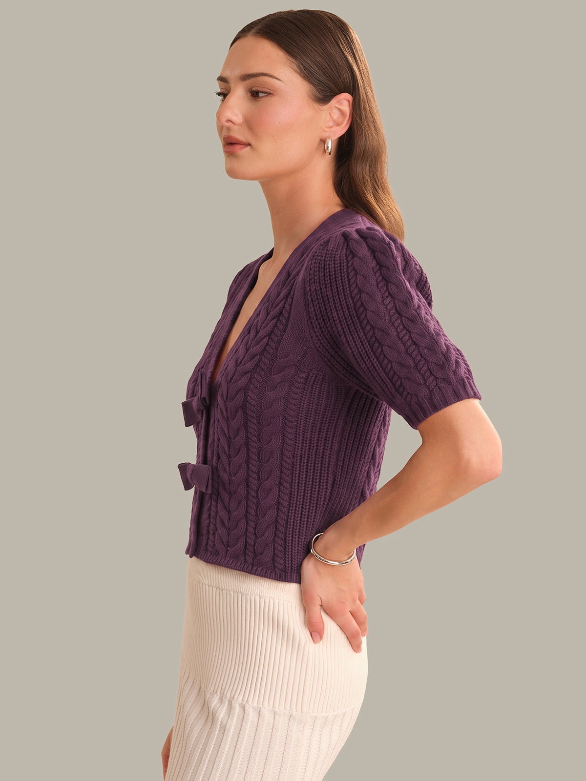 Woman wearing a purple cable knit cardigan against a gray background