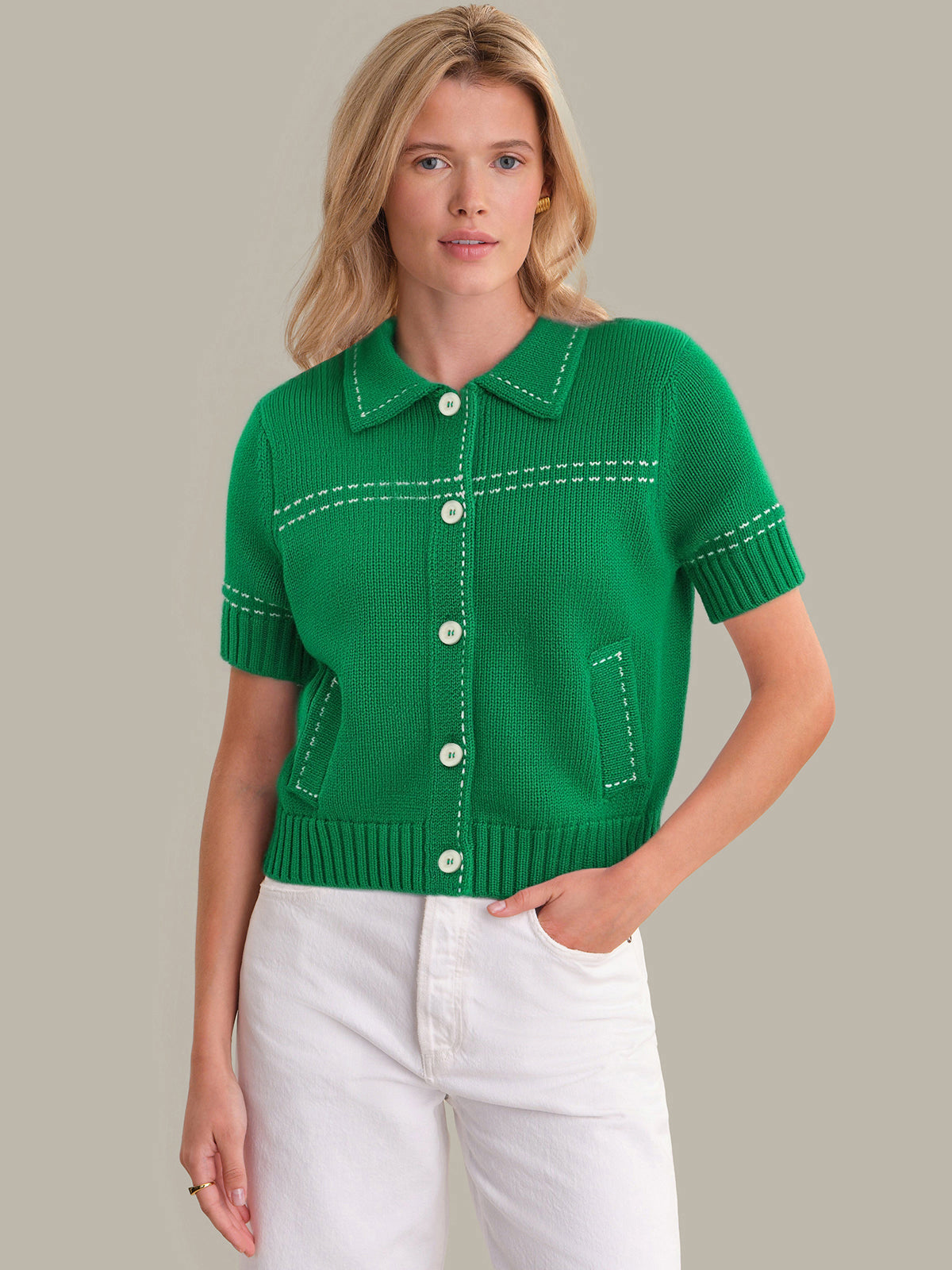 Woman wearing a green knitted short-sleeve cardigan with white pants on a neutral background