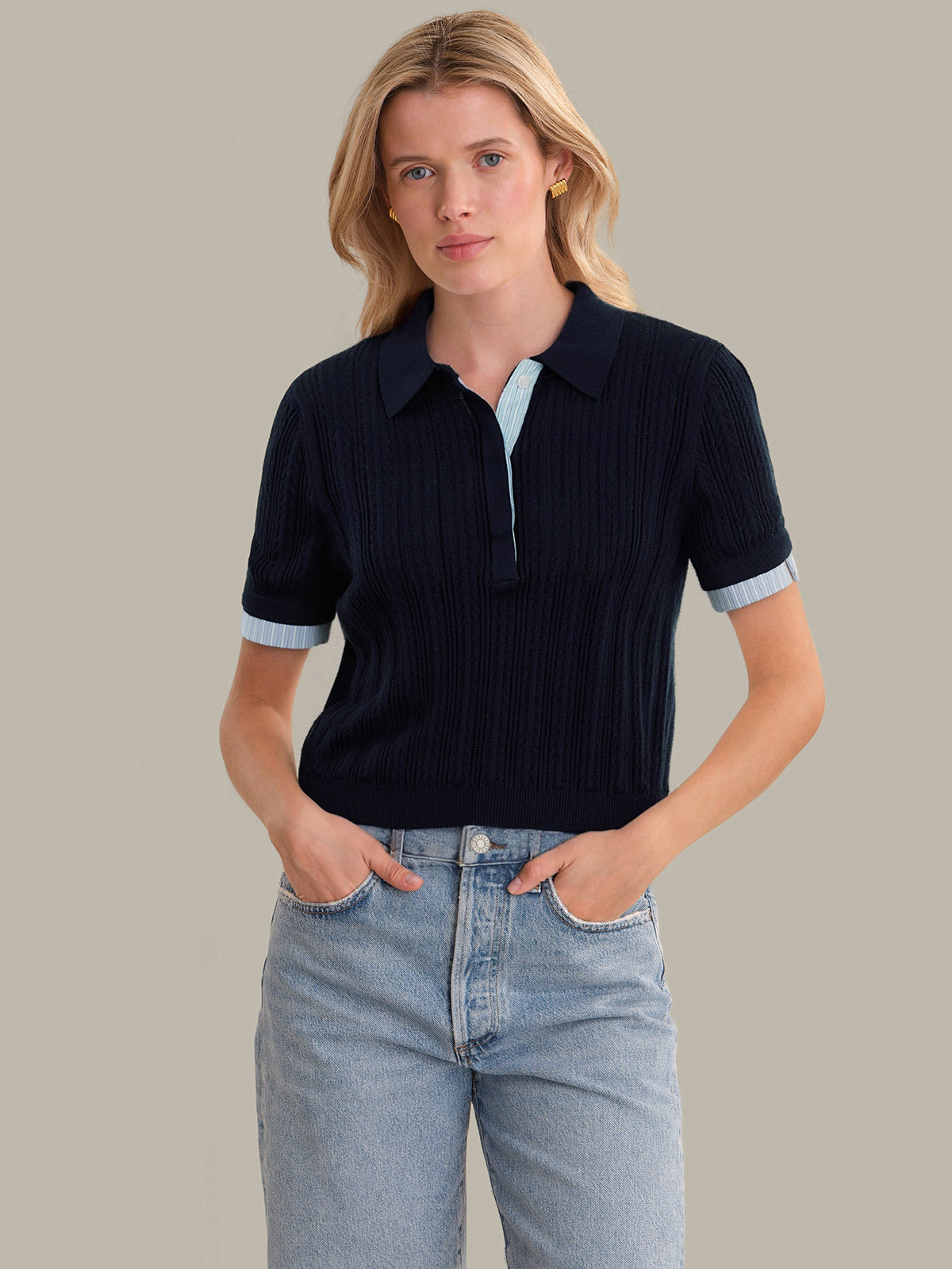 Woman wearing a dark blue ribbed polo shirt with light blue trim on a neutral background