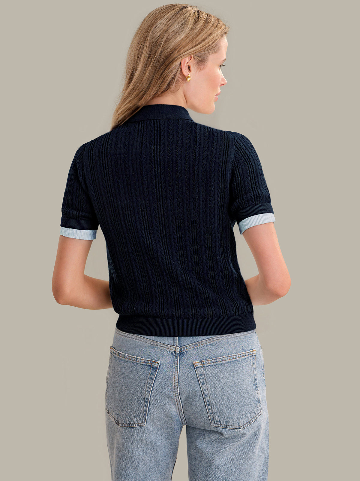 Woman wearing a dark blue ribbed sweater and light blue jeans on a beige background