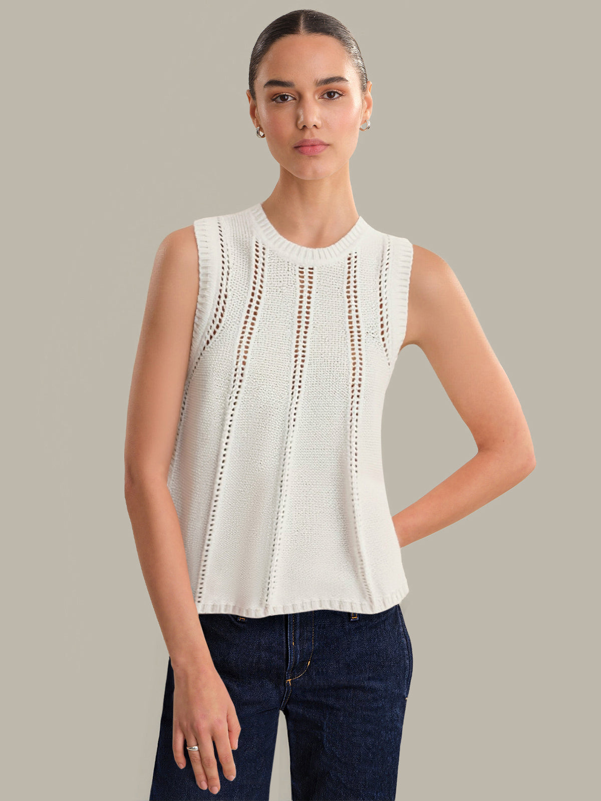 Woman wearing a white sleeveless top with lace details on a gray background