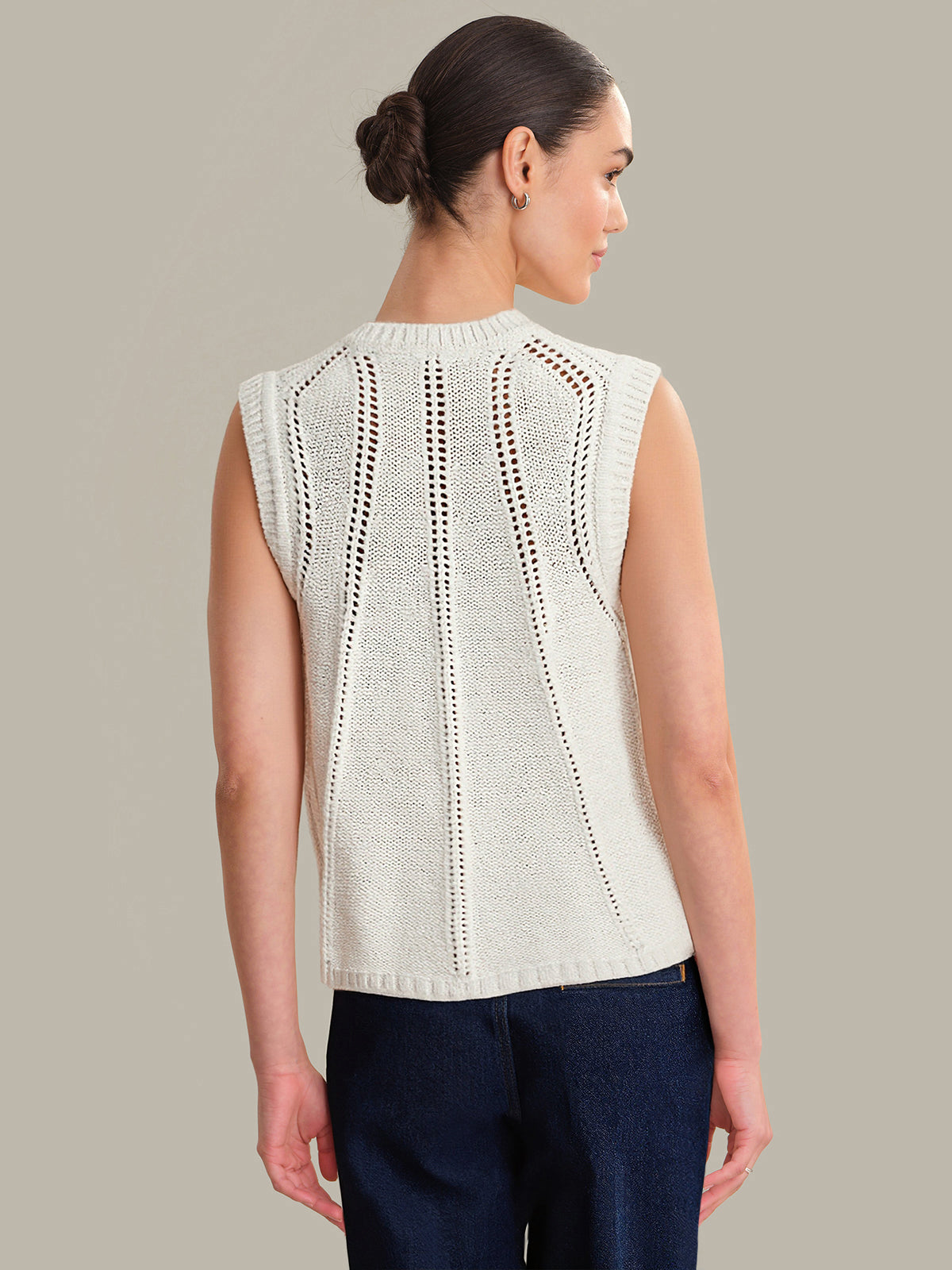 Woman wearing a light-colored sleeveless knitted top against a neutral background