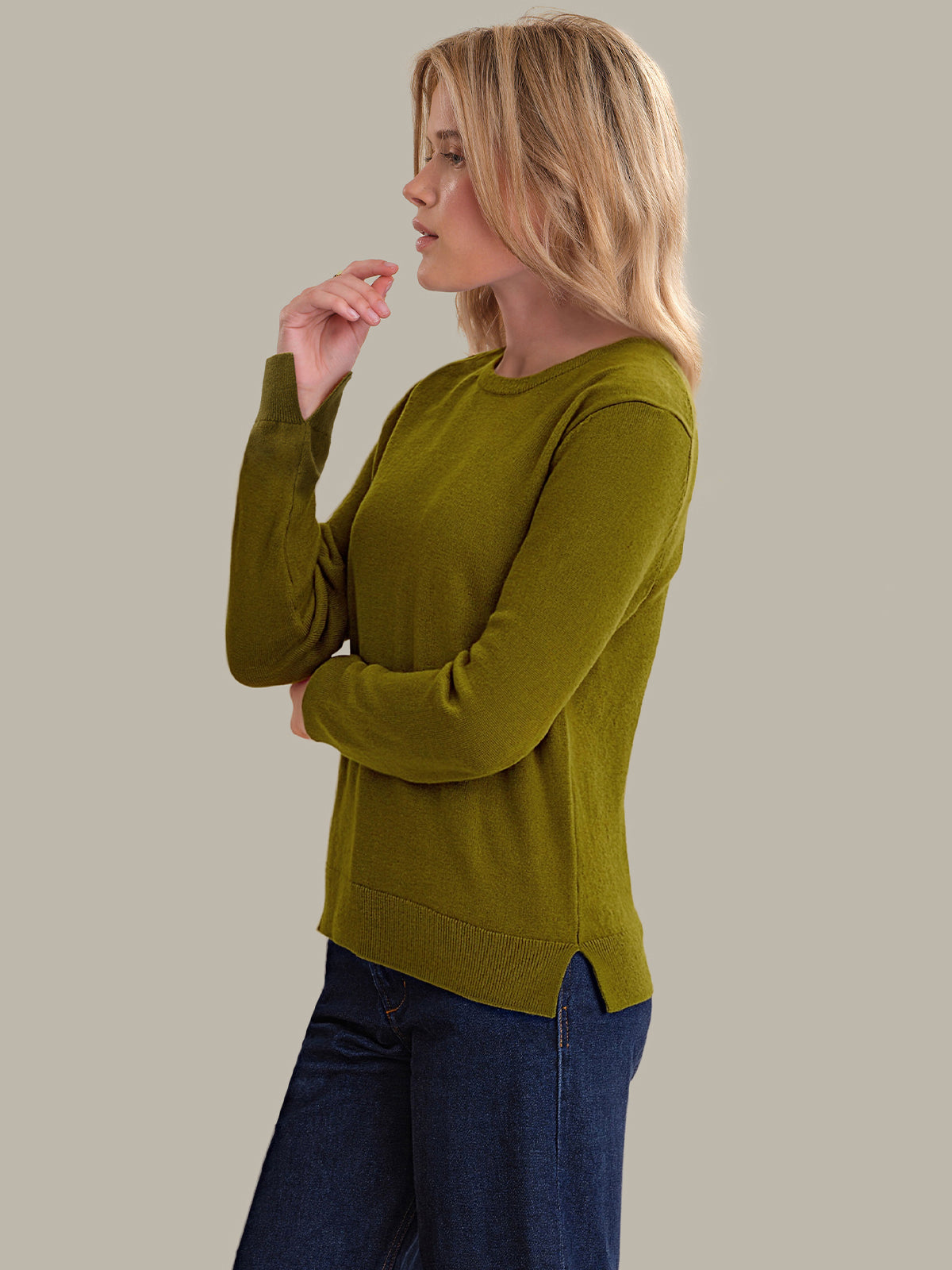 Woman wearing a green sweater and blue jeans against a beige background