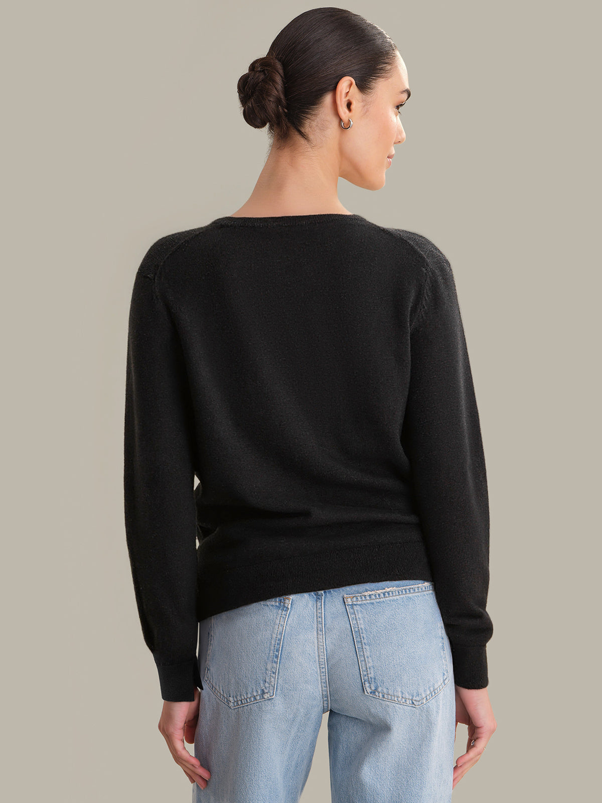 Person wearing a black sweater and light blue jeans against a neutral background