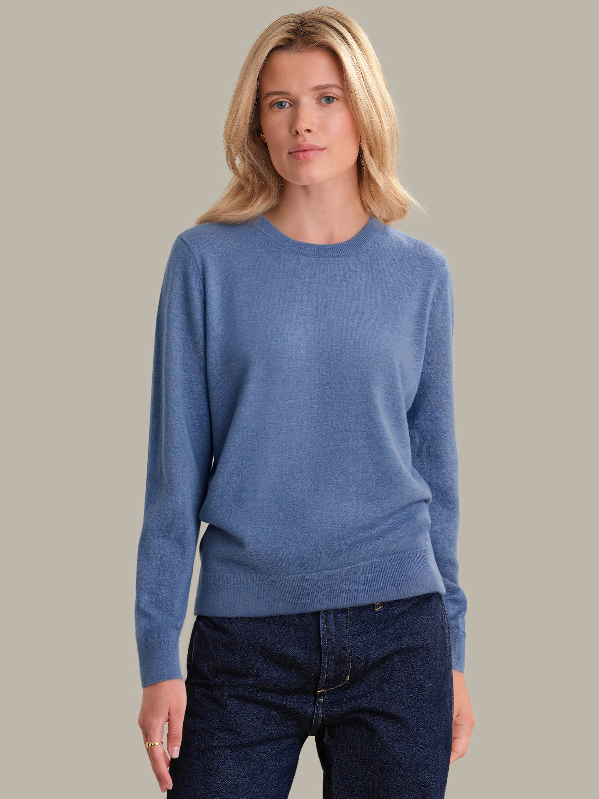 Woman wearing a blue sweater and dark jeans against a plain background