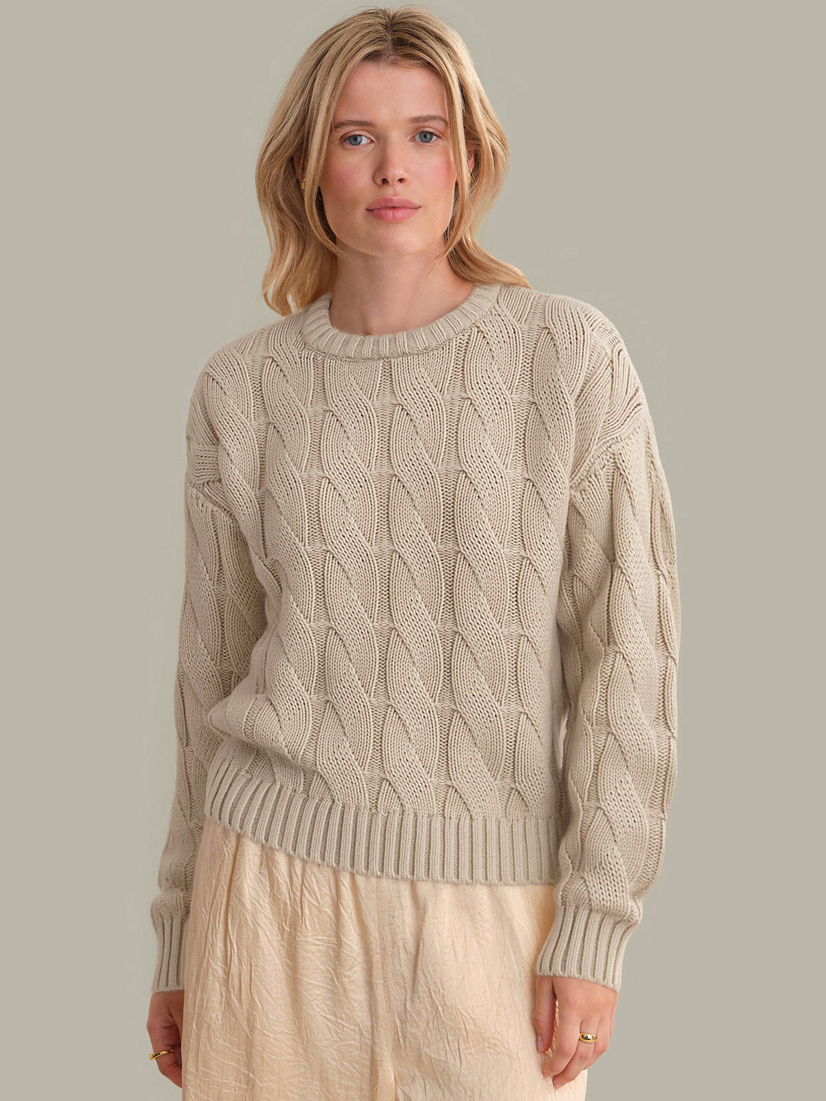 Woman wearing a beige cable knit sweater against a plain background