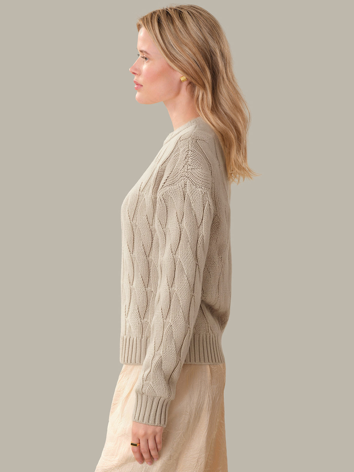Woman wearing a beige cable knit sweater against a plain background