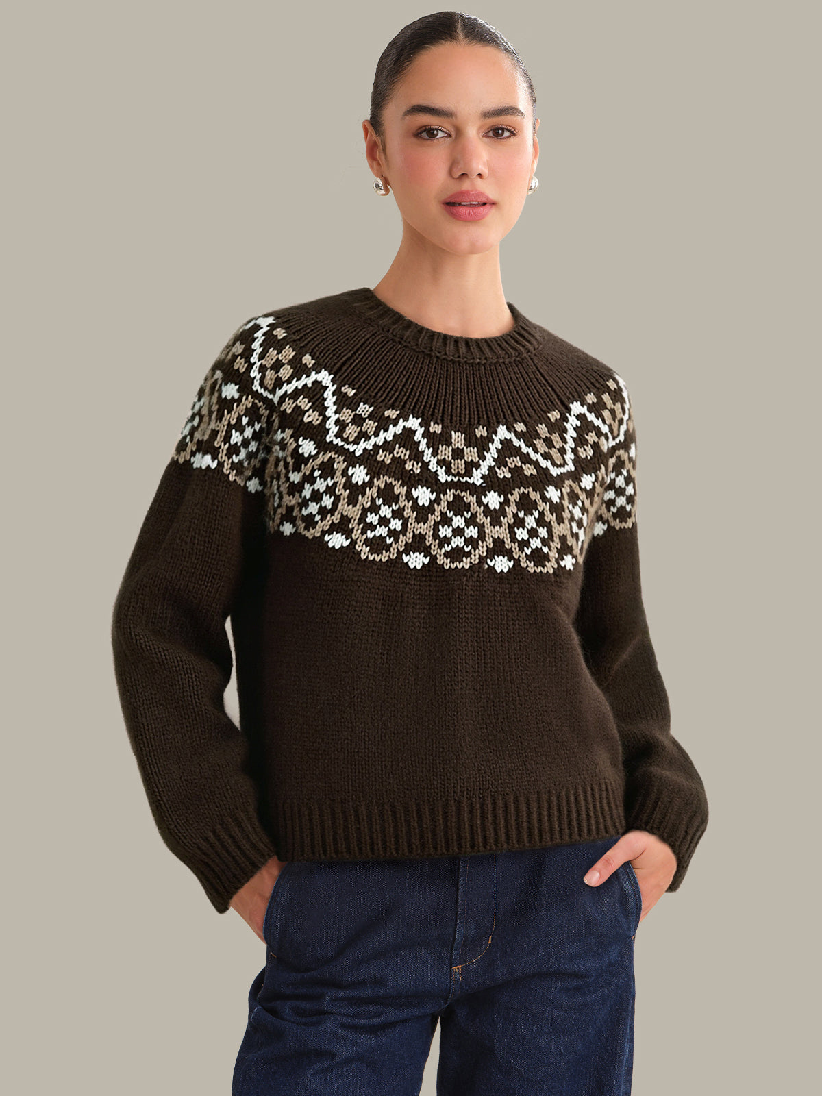 Woman wearing a brown sweater with a patterned yoke against a gray background