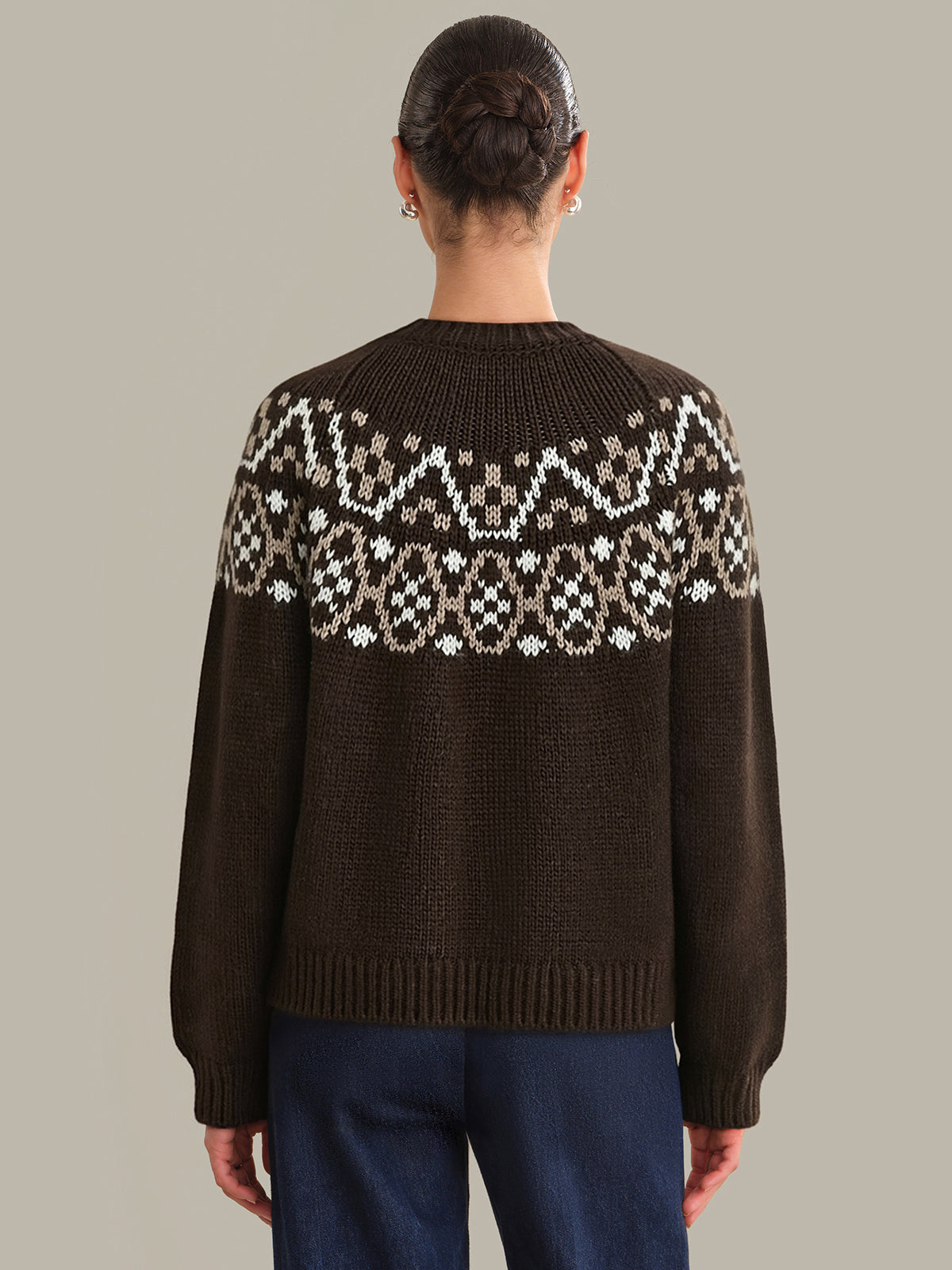 Person wearing a brown sweater with a patterned back design on a plain background