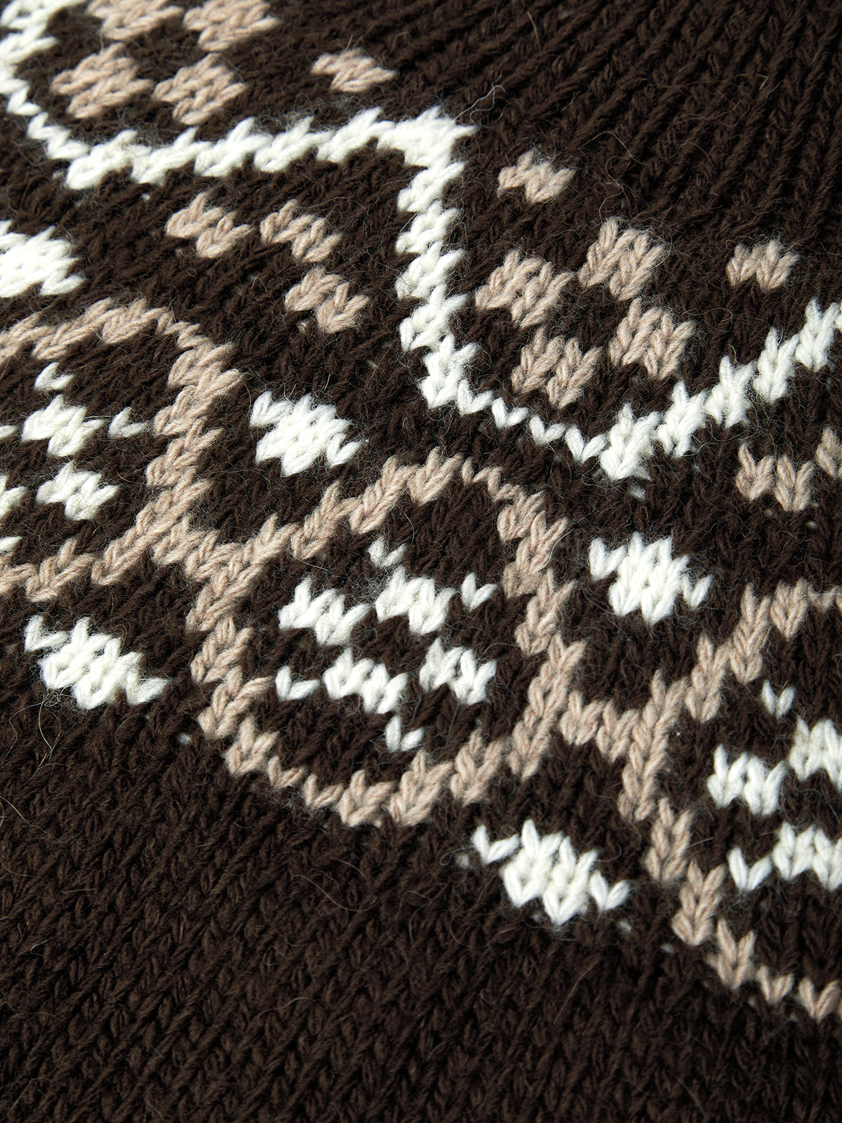 Close-up of a knitted fabric with a geometric pattern in brown, beige, and white.