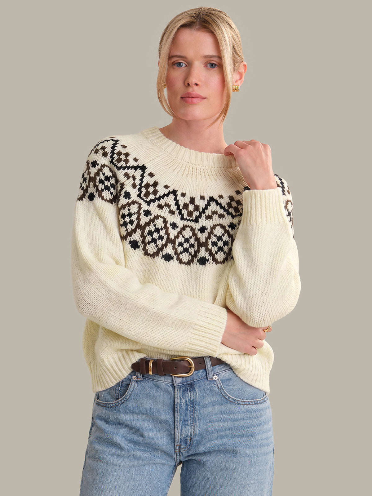 Woman wearing a cream sweater with black pattern and blue jeans on a gray background