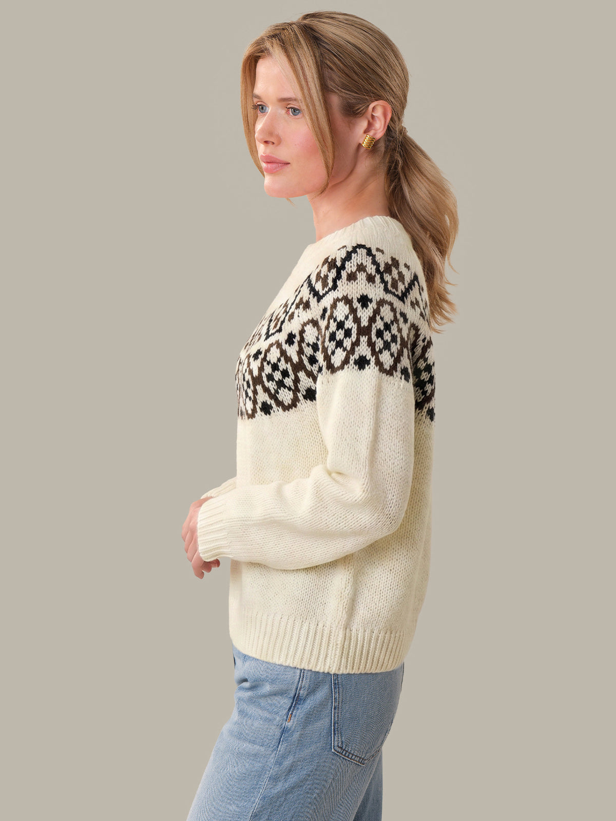 Woman wearing a cream sweater with black pattern on a plain background