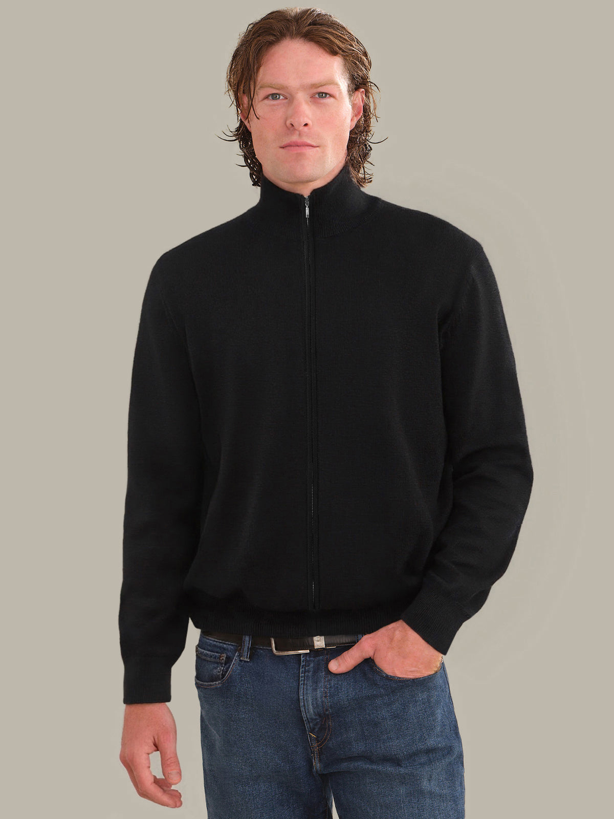 Man wearing a black zip-up sweatshirt and blue jeans against a plain background