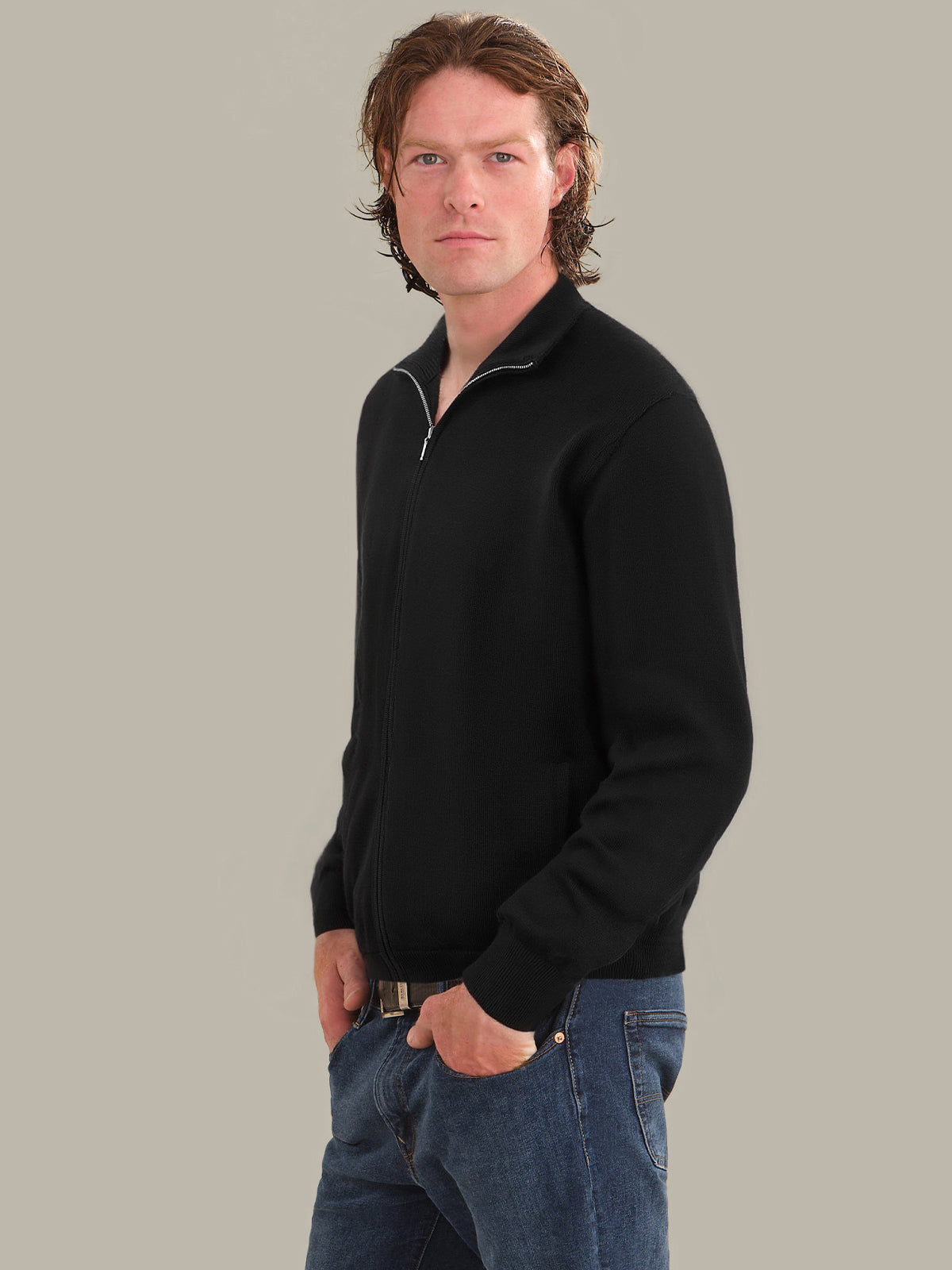 Man wearing a black quarter-zip sweater and blue jeans against a gray background