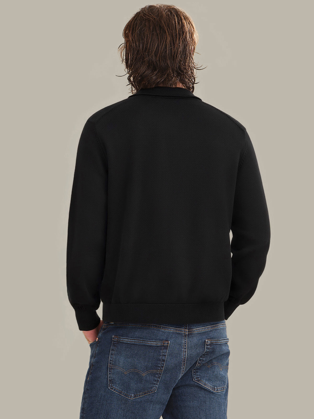 Person wearing a black sweater and blue jeans on a plain background