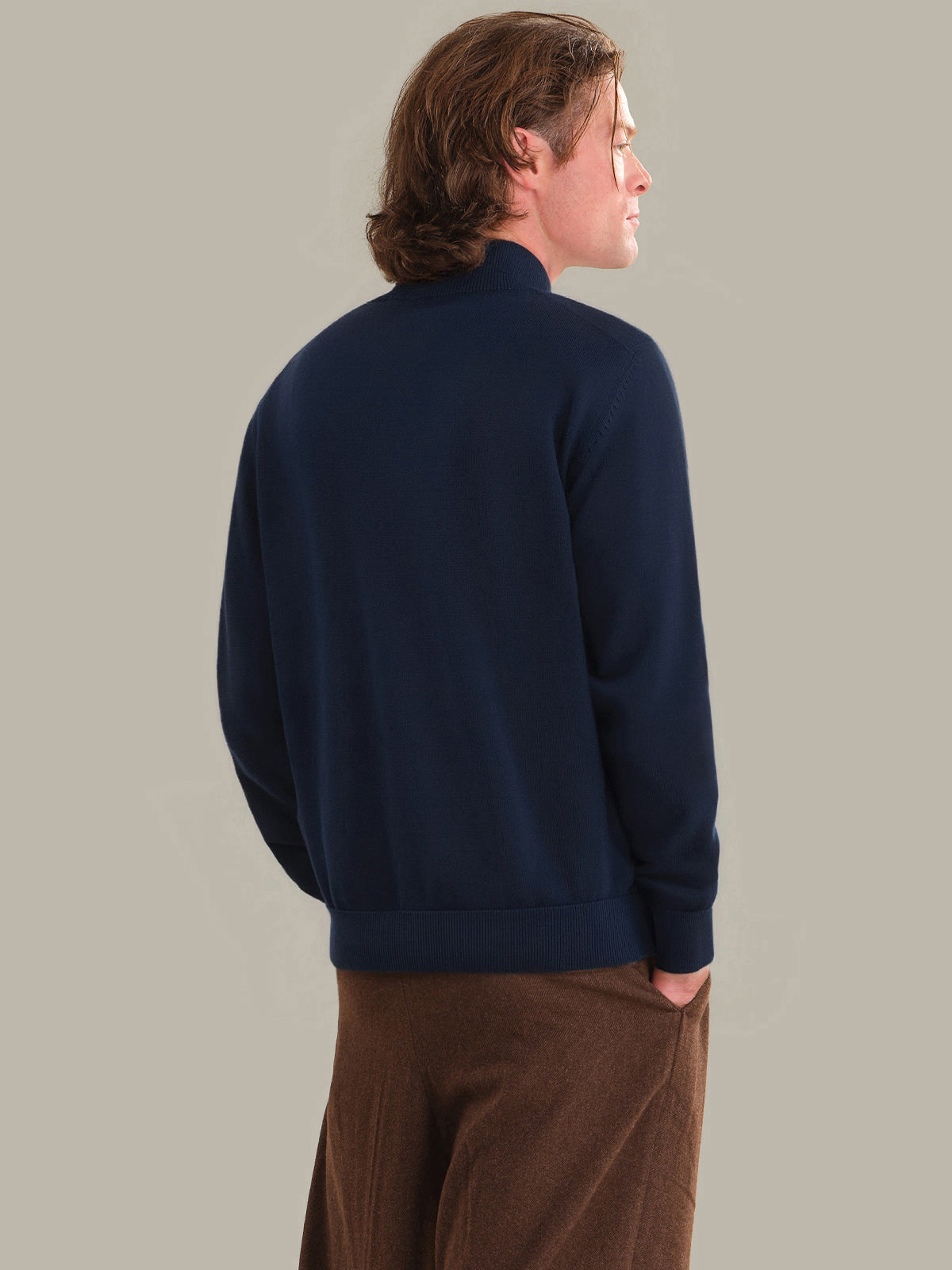 Person wearing a navy blue sweater and brown pants against a plain background