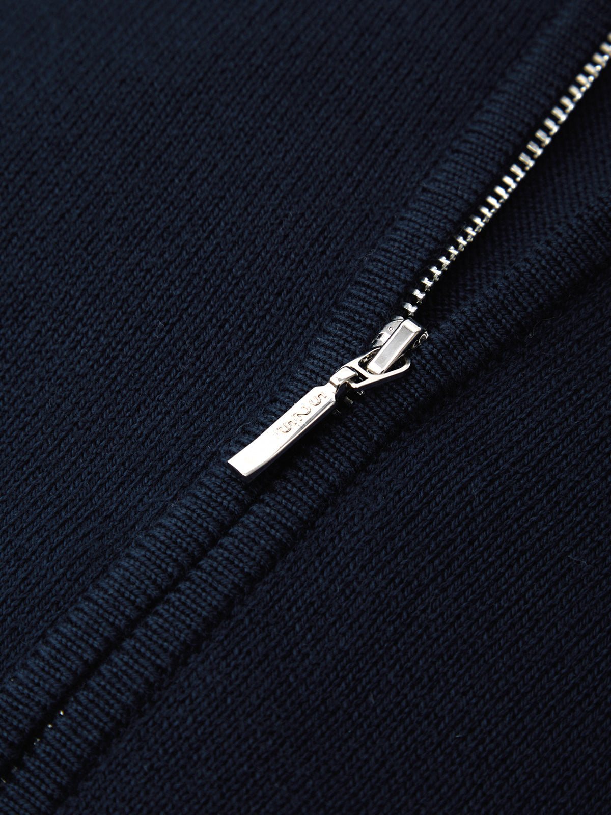 Close-up of a navy blue zipper with a silver pull on a matching fabric background