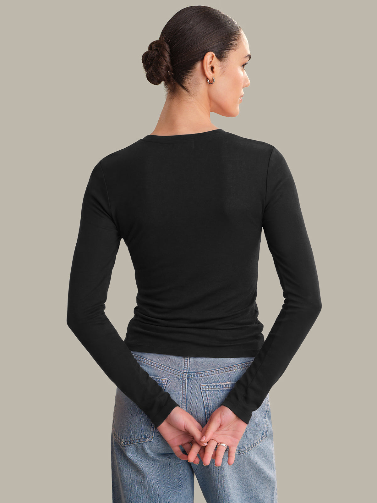 Person wearing a black long-sleeve top and blue jeans on a plain background