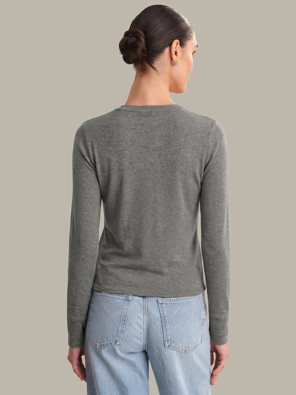 Woman wearing a gray long-sleeve shirt and light blue jeans on a plain background