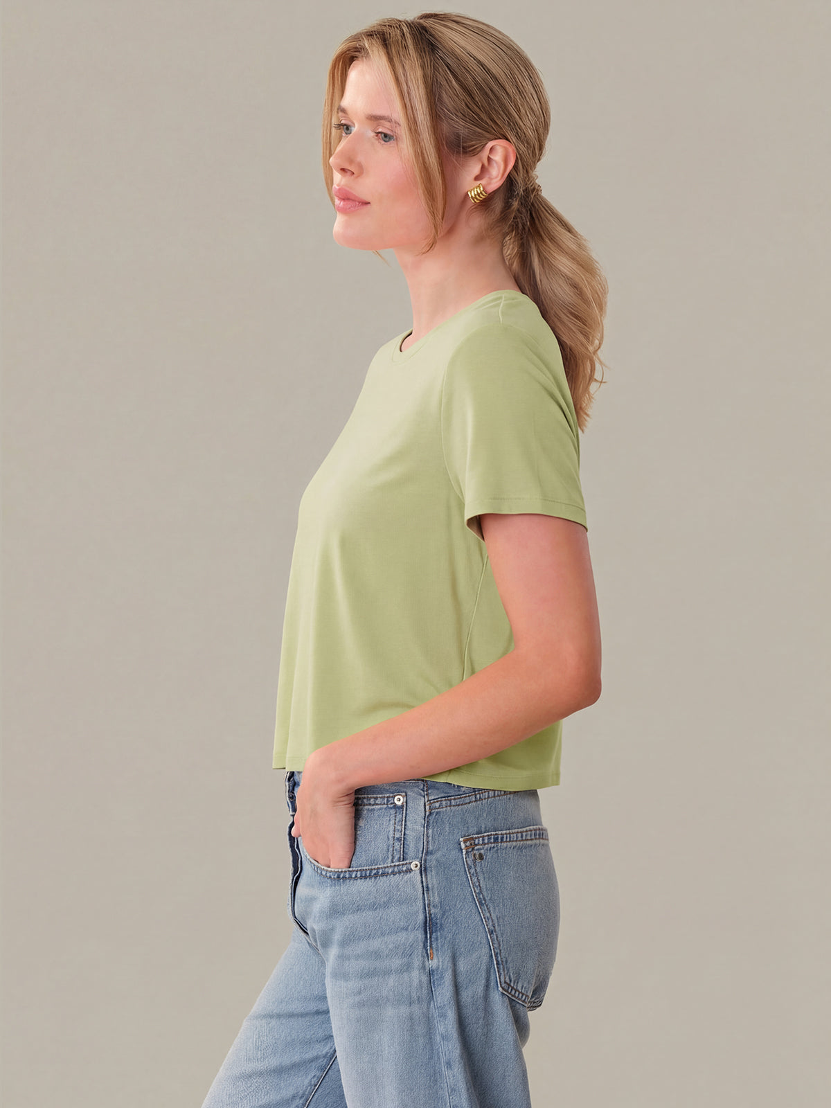 Woman wearing a light green t-shirt and blue jeans against a plain background