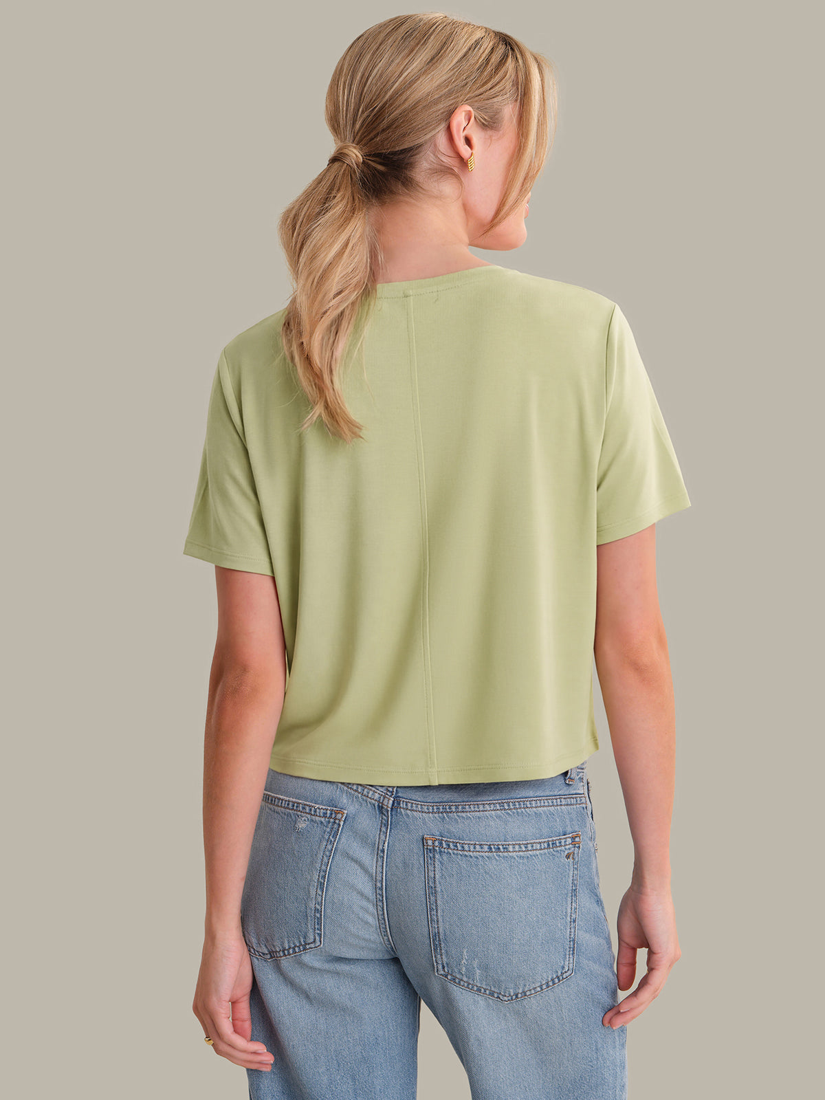 Person wearing a light green t-shirt and blue jeans on a plain background