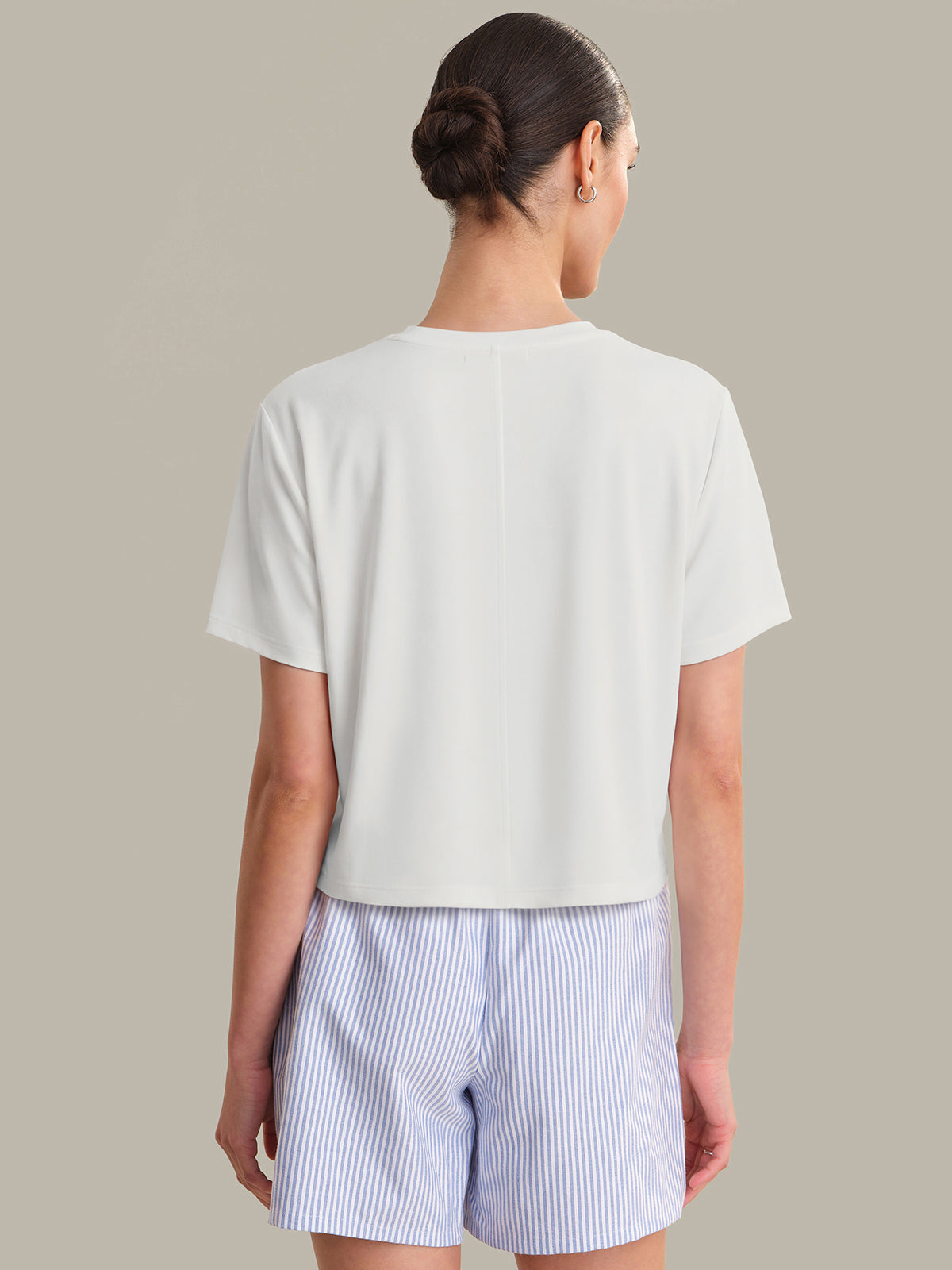 Woman wearing a light-colored t-shirt and striped shorts on a plain background