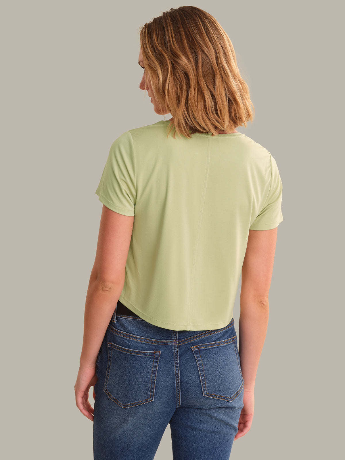 Person wearing a light green t-shirt and blue jeans on a plain background