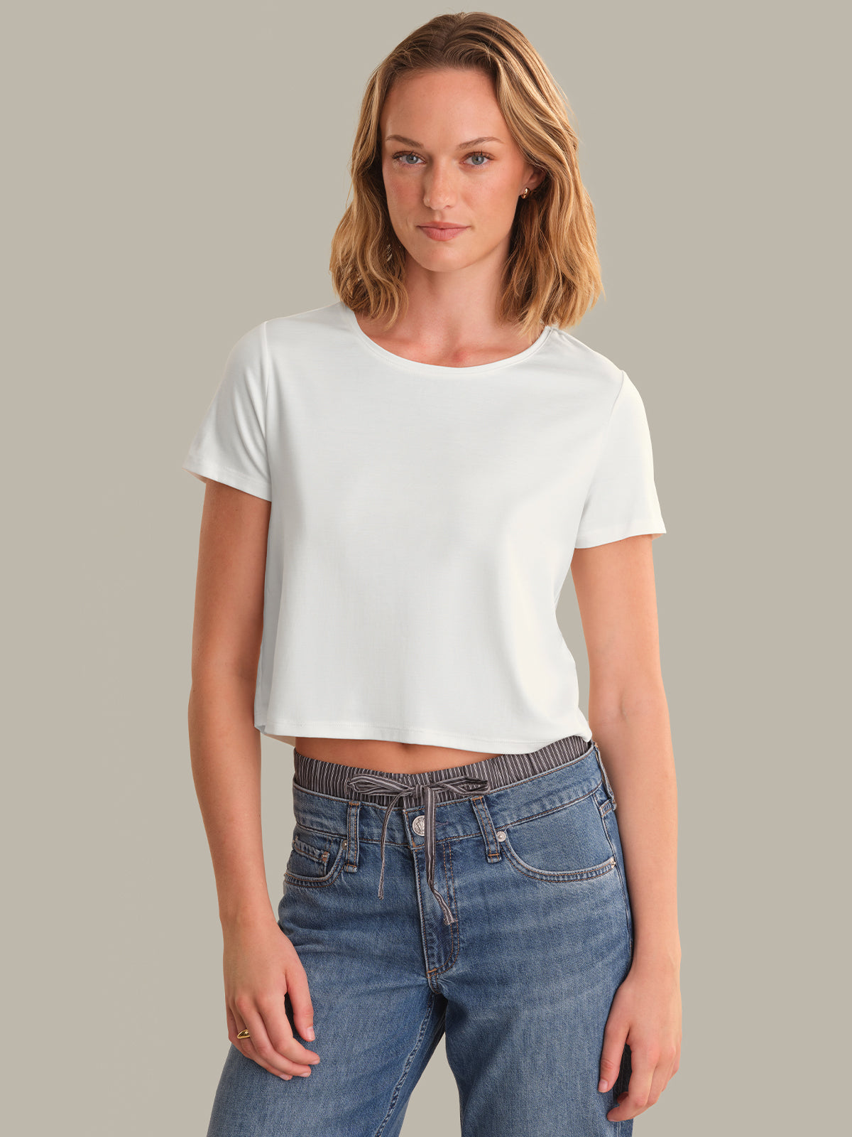 Woman wearing a white crop top and blue jeans against a plain background