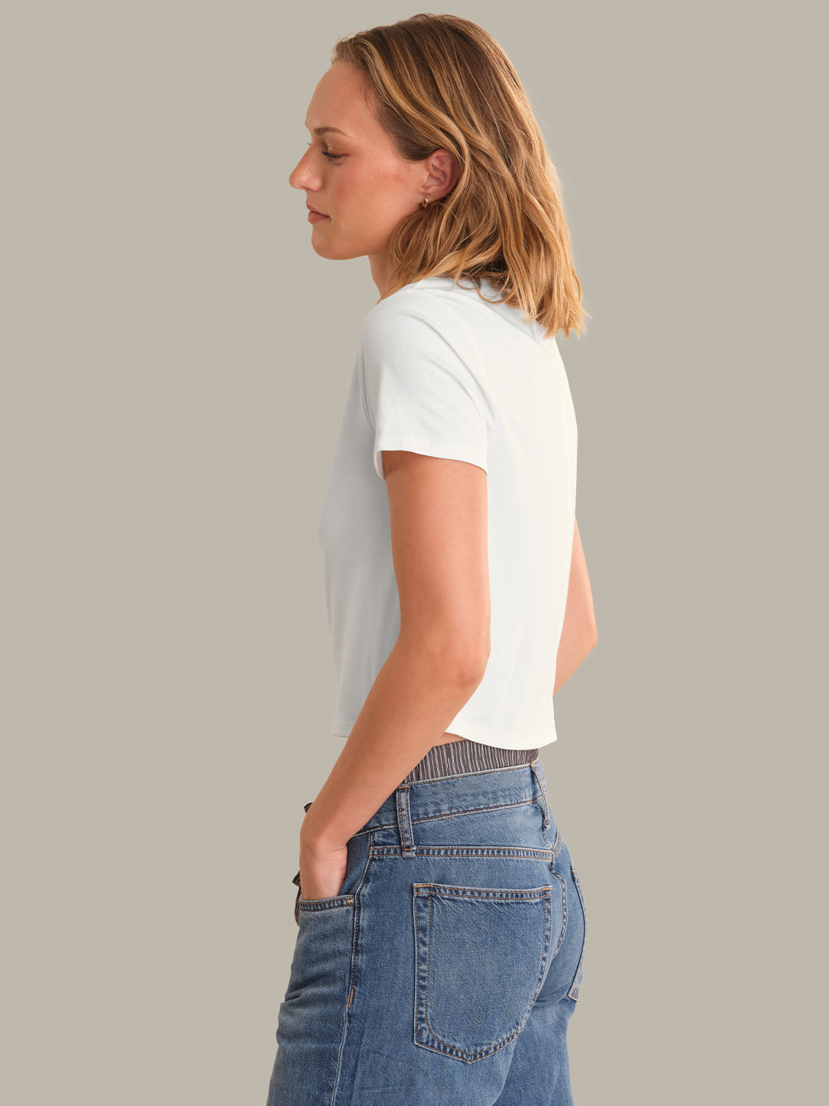 Woman wearing a white t-shirt and blue jeans against a gray background