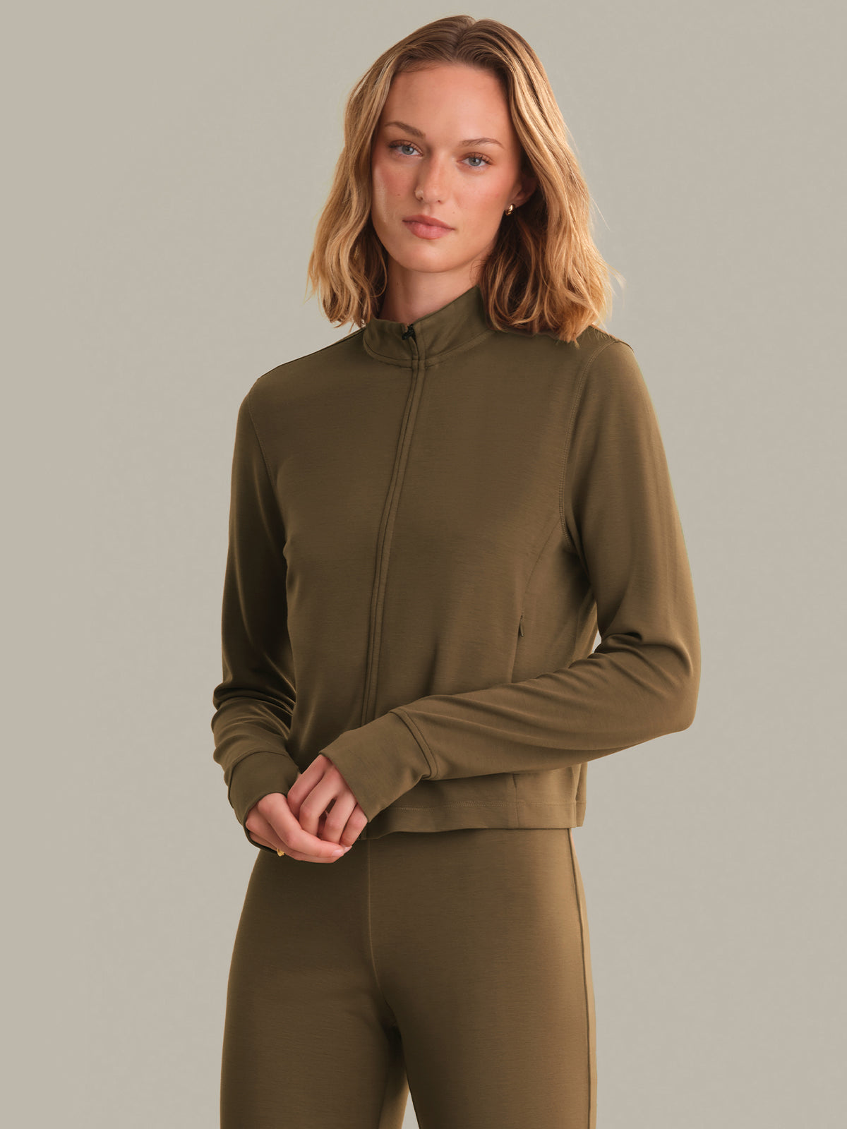 Woman wearing an brown zip-up top and leggings against a gray background