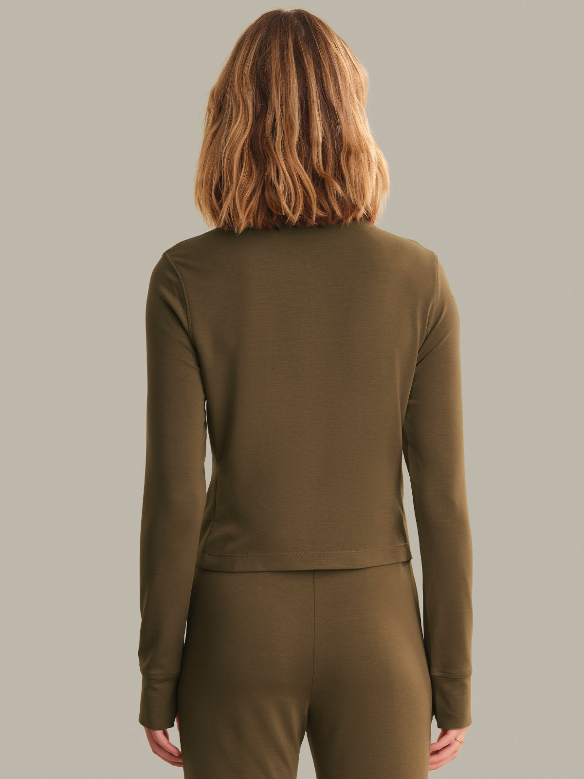 Person wearing a brown long-sleeve top and pants on a gray background