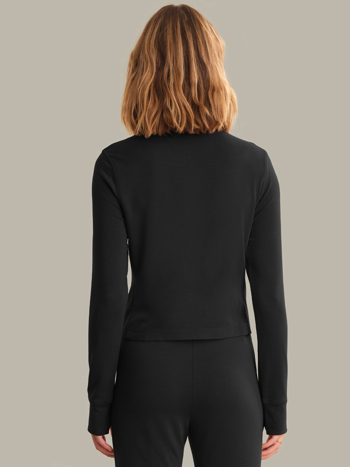 Person wearing a black long-sleeve top and pants on a gray background