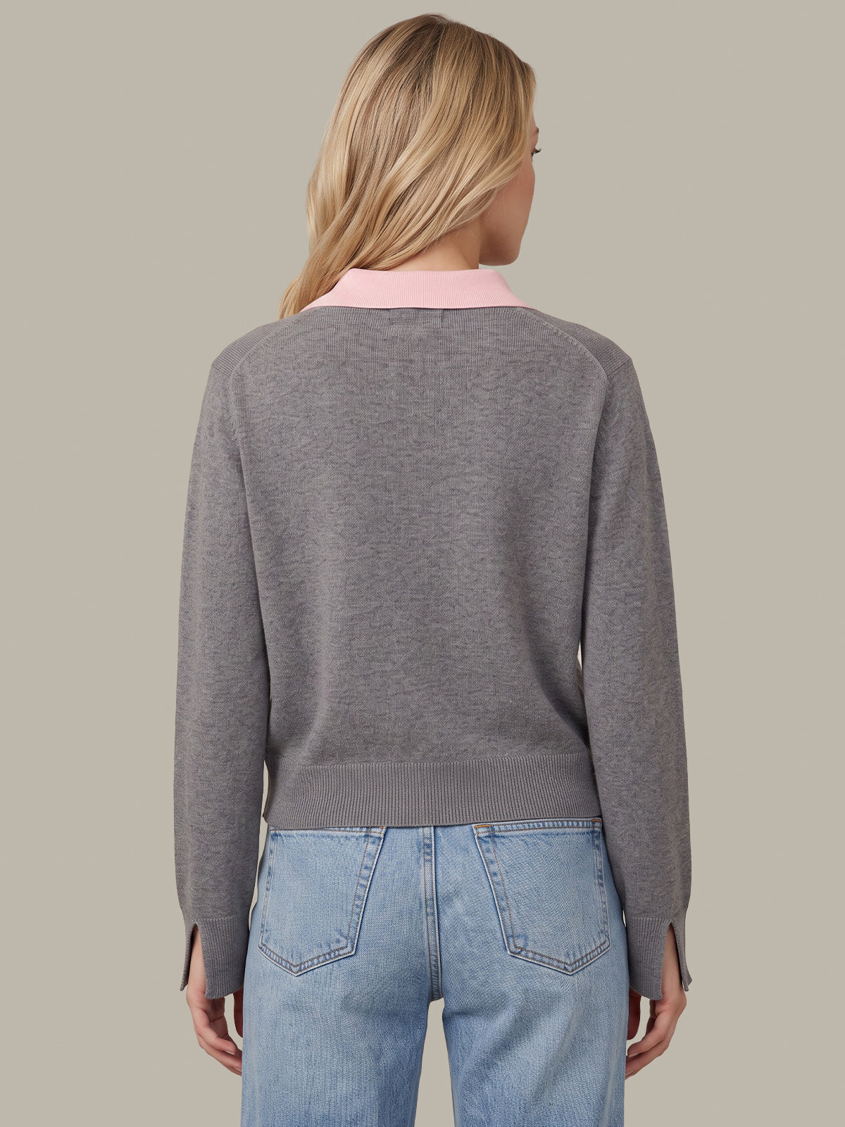 A woman shown from the back wearing a heather gray knit sweater with a contrasting light pink collar, paired with light blue jeans, against a solid taupe background.