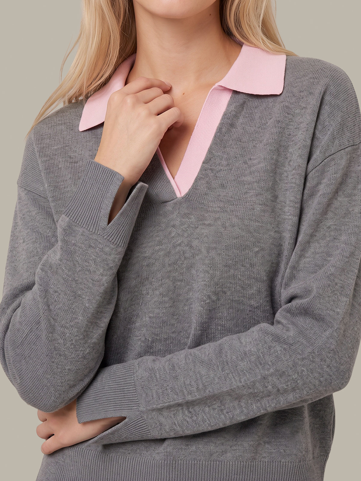 A close-up of a woman wearing a heather gray knit sweater with a contrasting light pink collar, set against a solid neutral background.